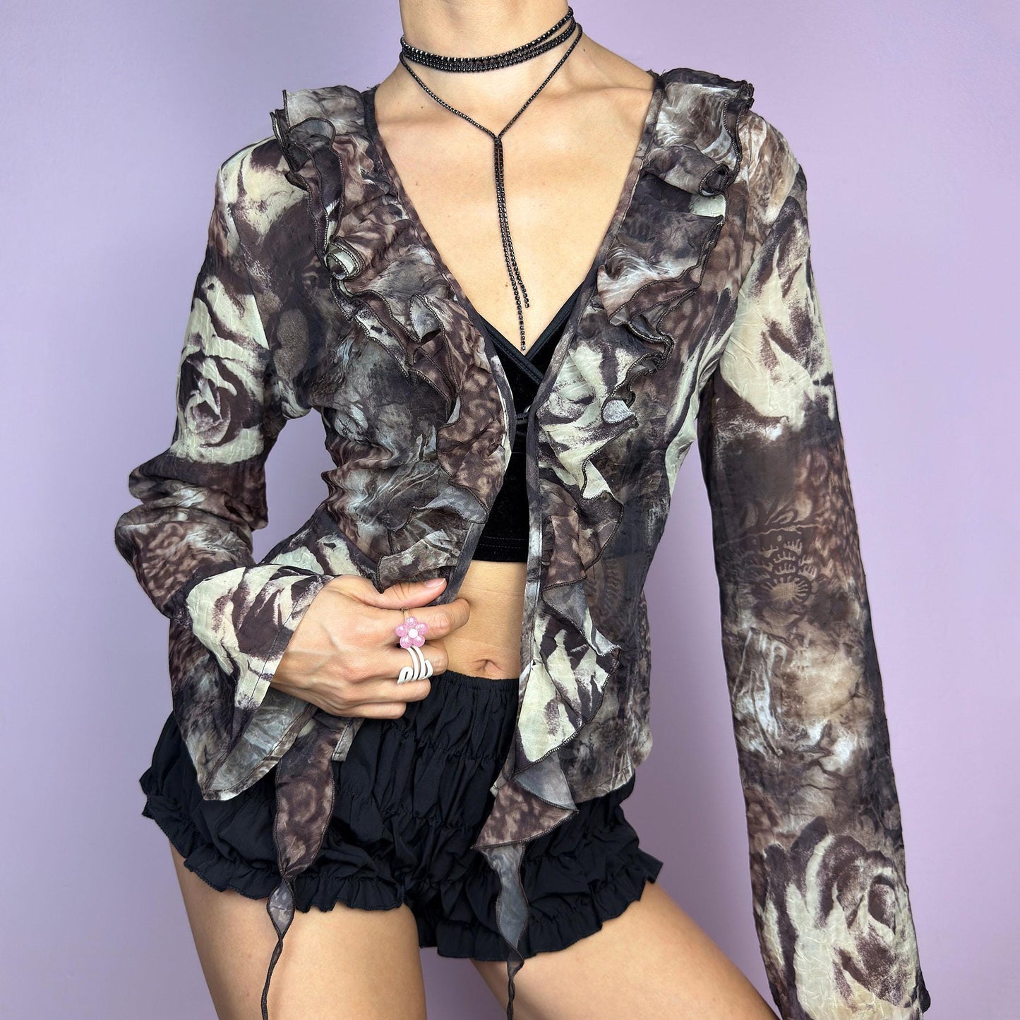 The Y2K Printed Ruffle Blouse is a stunning vintage 2000s romantic piece crafted from sheer, lightweight fabric in brown tones and featuring a blend of earthy hues in a rose-patterned print. adult world shop