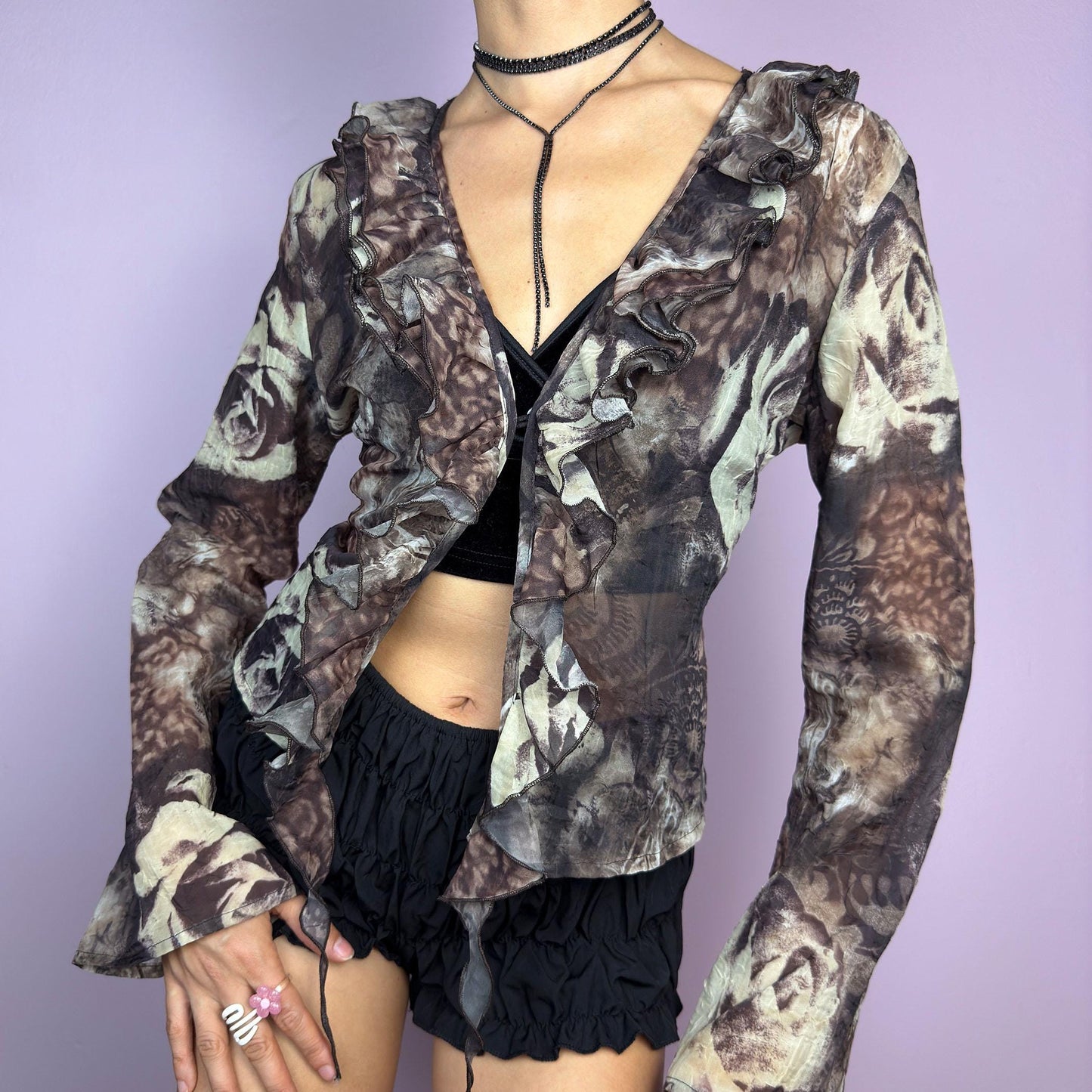 The Y2K Printed Ruffle Blouse is a stunning vintage 2000s romantic piece crafted from sheer, lightweight fabric in brown tones and featuring a blend of earthy hues in a rose-patterned print. adult world shop