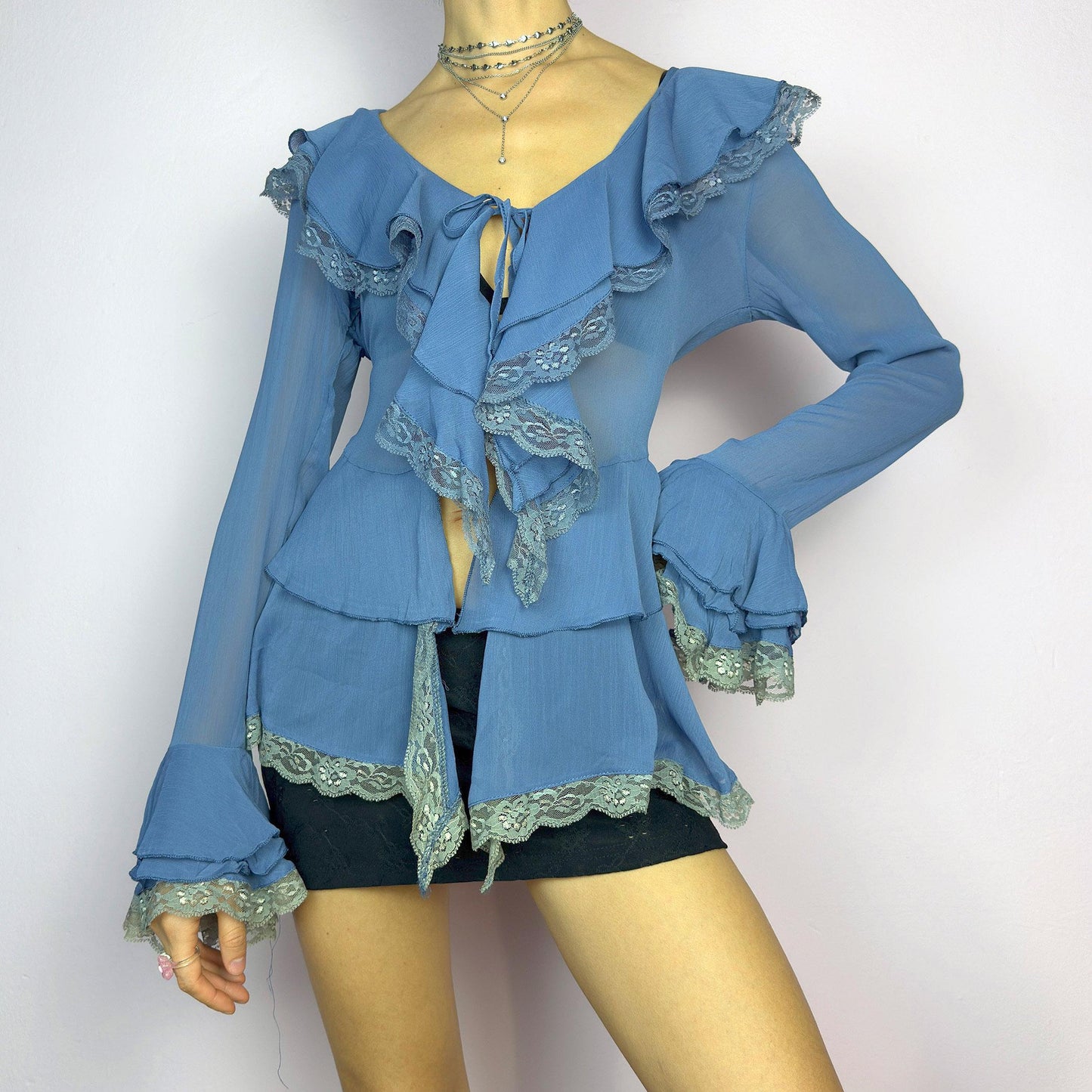 The Y2K Blue Ruffle Blouse is a dreamy vintage 2000s piece with a romantic and ethereal aesthetic. Crafted from a sheer, lightweight fabric in a soft blue shade, this blouse features cascading ruffles with delicate lace trim. adult world shop