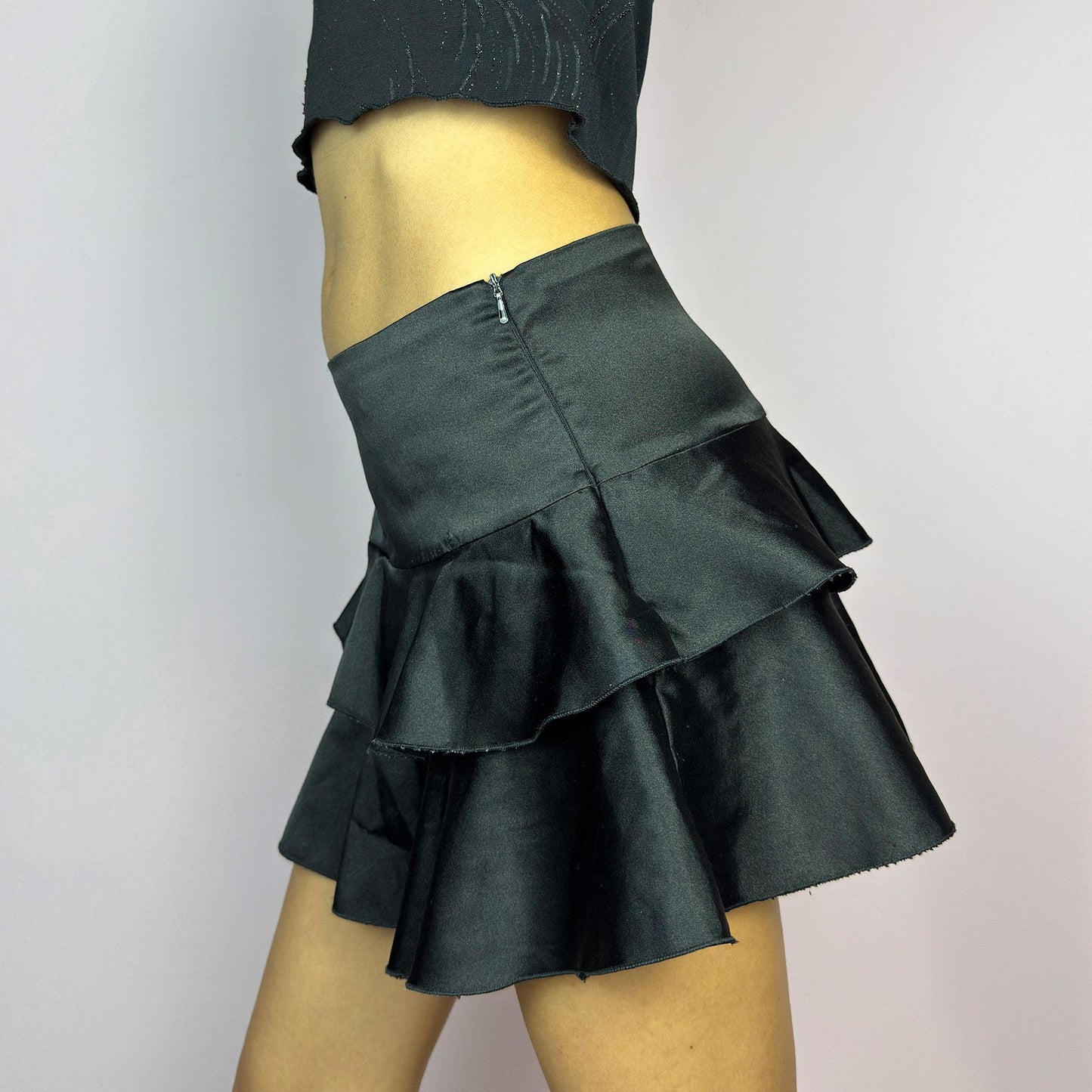 The Y2K Black Ruffle Satin Mini Skirt is a vintage 2000s piece made from a sleek satin-style stretchy fabric featuring layered ruffles, low rise design and a side zipper closure. Ideal for a night-out outfit. adult world shop