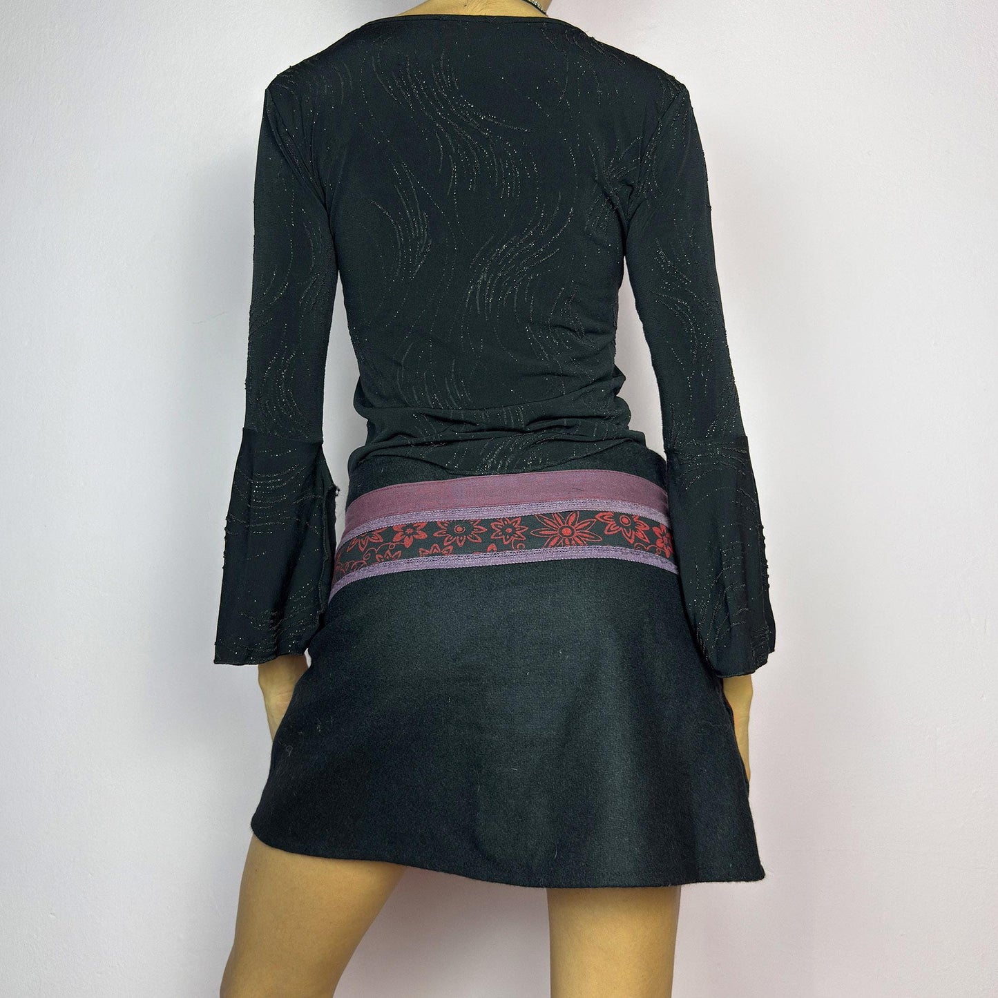 The Y2K Black Wrap Mini Skirt is a vintage 2000s piece featuring a unique wrap design with an adjustable Velcro waist for a customizable fit. Made from a thick fabric, the skirt has a contrasting waistband with floral details. adult world shop