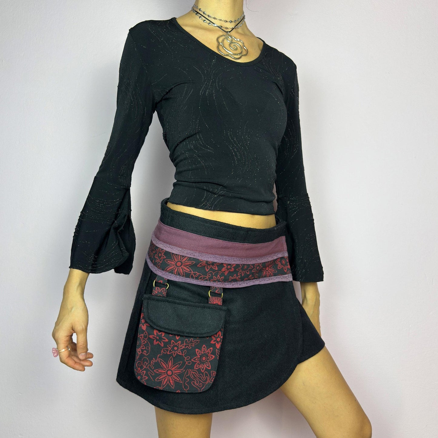 The Y2K Black Wrap Mini Skirt is a vintage 2000s piece featuring a unique wrap design with an adjustable Velcro waist for a customizable fit. Made from a thick fabric, the skirt has a contrasting waistband with floral details. adult world shop