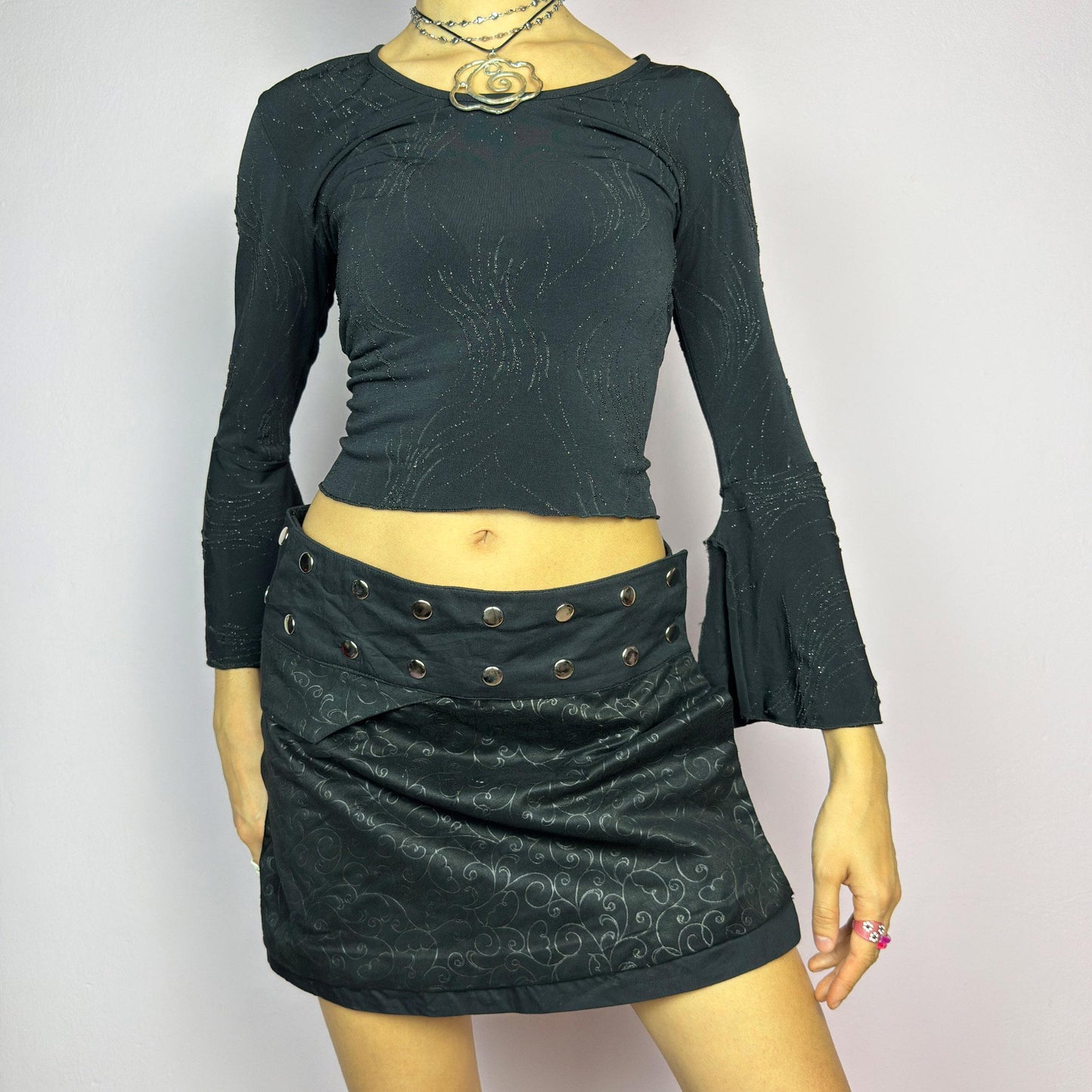 The Y2K Wrap Mini Black Skirt is a vintage 2000s piece featuring a snap-button closure on the waistband for an adjustable fit. Made from a thick fabric with a subtle floral pattern design, its wrap silhouette. adult world shop