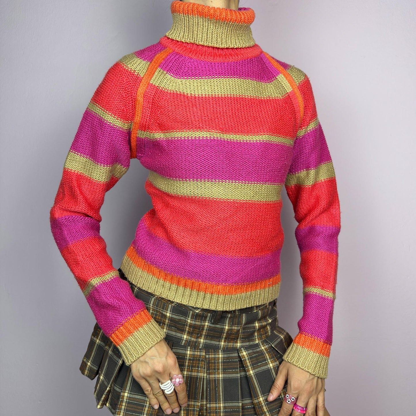 The Y2K Turtleneck Striped Sweater is a vintage 2000s staple featuring a bold striped design in vibrant tones. Crafted from a knit fabric, it has a cozy ribbed turtleneck, cuffs, and hem for a snug fit. adult world shop