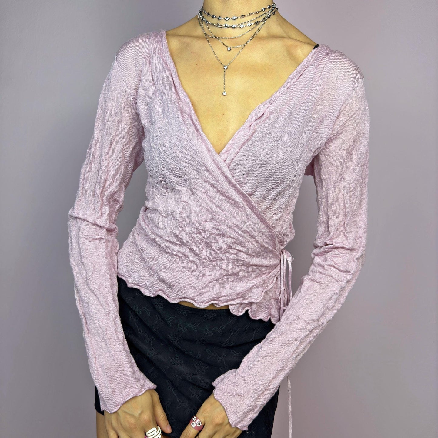 The Y2K Pink Wrap Tie Cardigan is a vintage 2000s delicate and feminine piece featuring a light pink hue and a textured knit fabric. Its wrap-around design ties at the side, creating an adjustable and flattering fit. adult world shop
