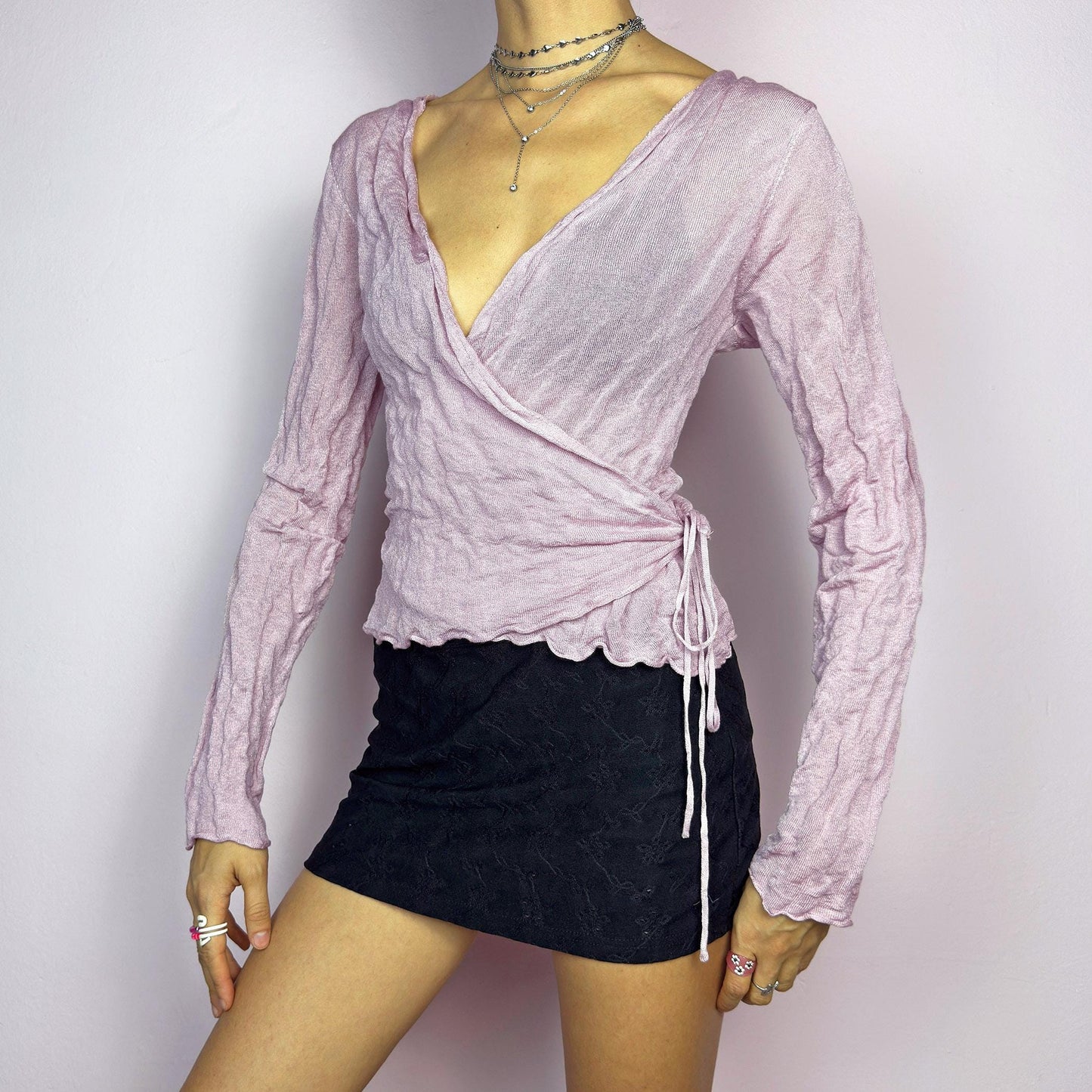 The Y2K Pink Wrap Tie Cardigan is a vintage 2000s delicate and feminine piece featuring a light pink hue and a textured knit fabric. Its wrap-around design ties at the side, creating an adjustable and flattering fit. adult world shop