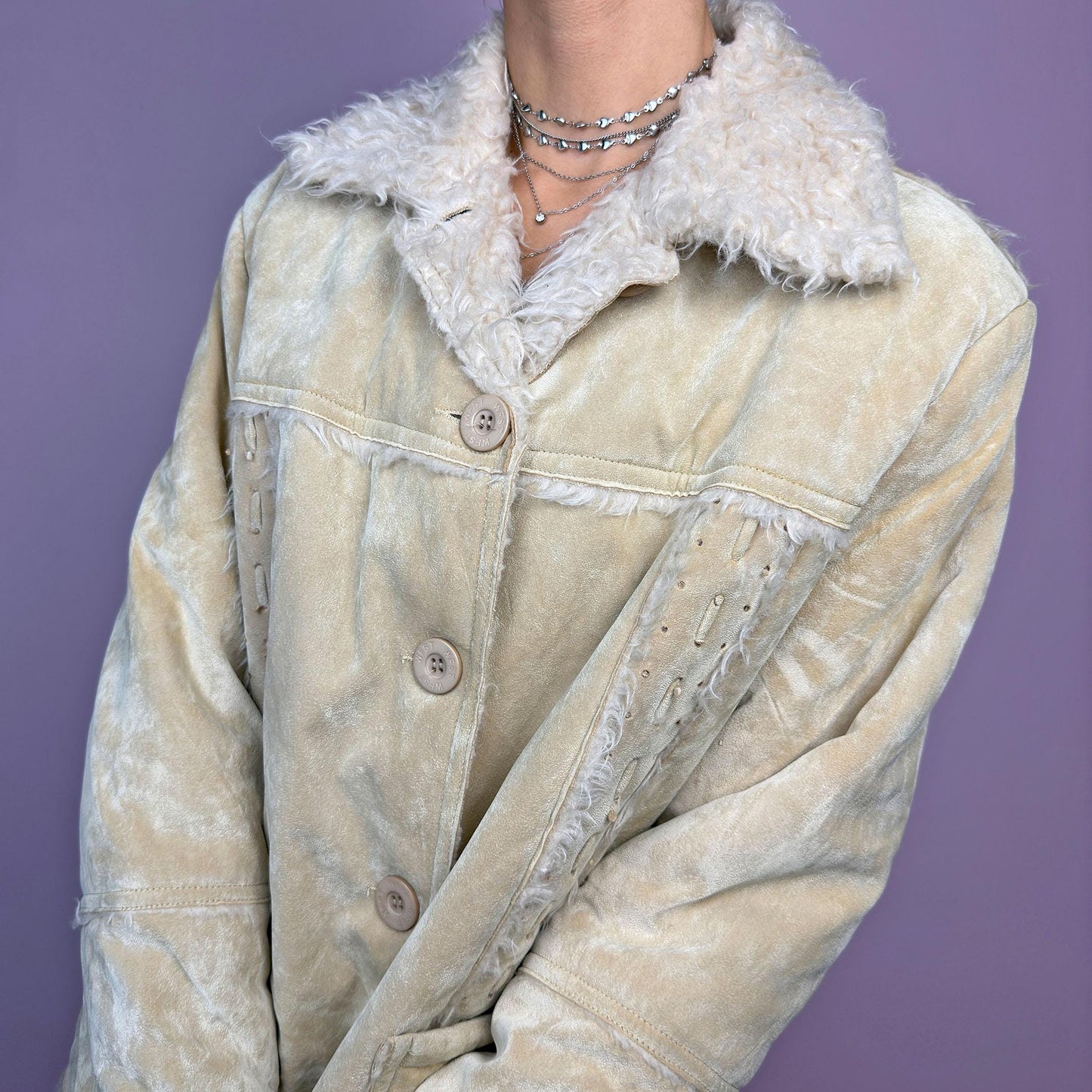 The Y2K Beige Faux Fur Suede Jacket is a vintage 2000s cozy outerwear piece featuring a soft faux suede finish in a beige tone, a faux shearling-lined collar and cuffs for added warmth, a button-front closure and pockets. adult world shop