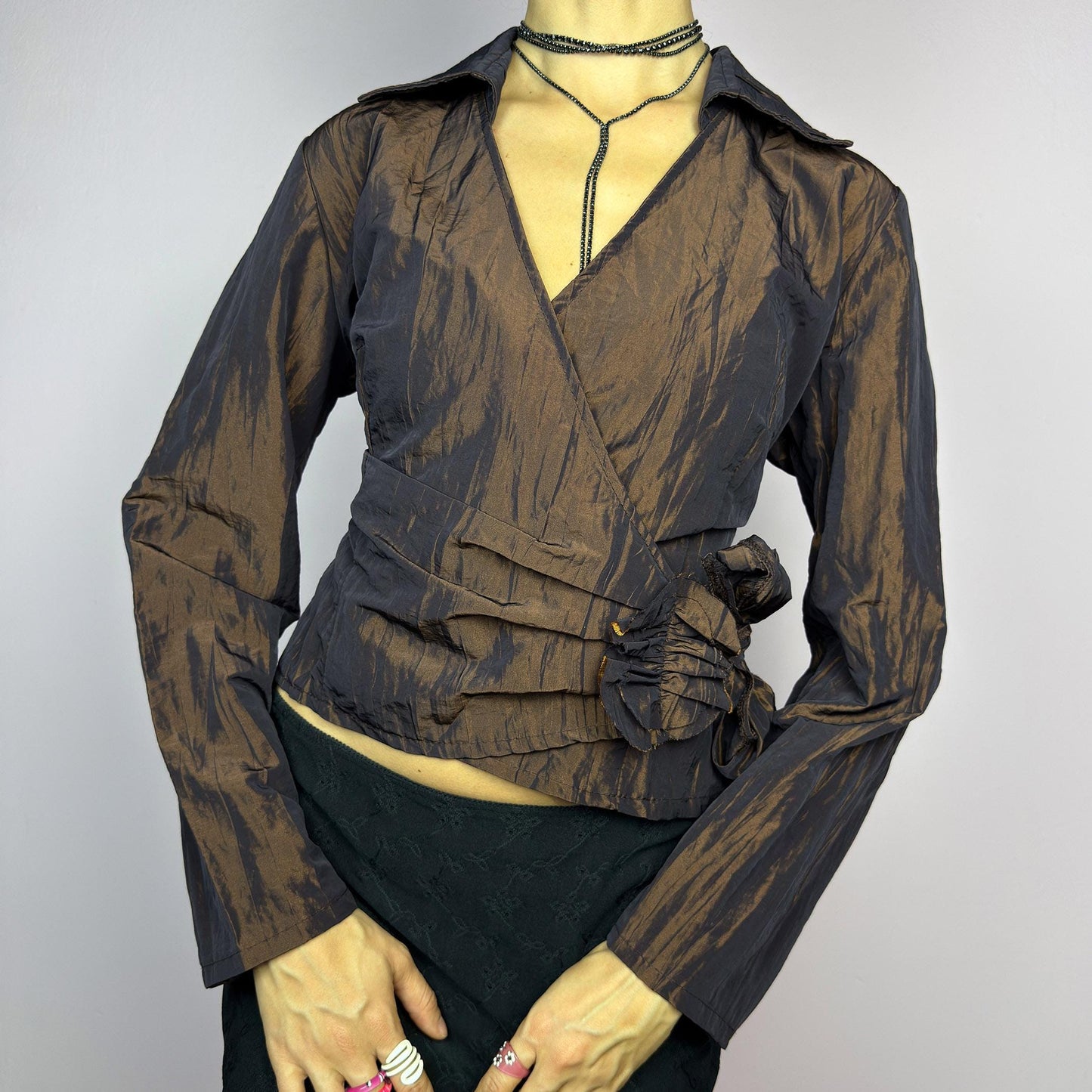 The Vintage 90s Brown Wrap Tie Blouse features a textured, crinkled fabric with a subtle iridescent finish, a flattering wrap design with a tie at the side. The deep brown tone adds versatility, while the structured collar. adult world shop