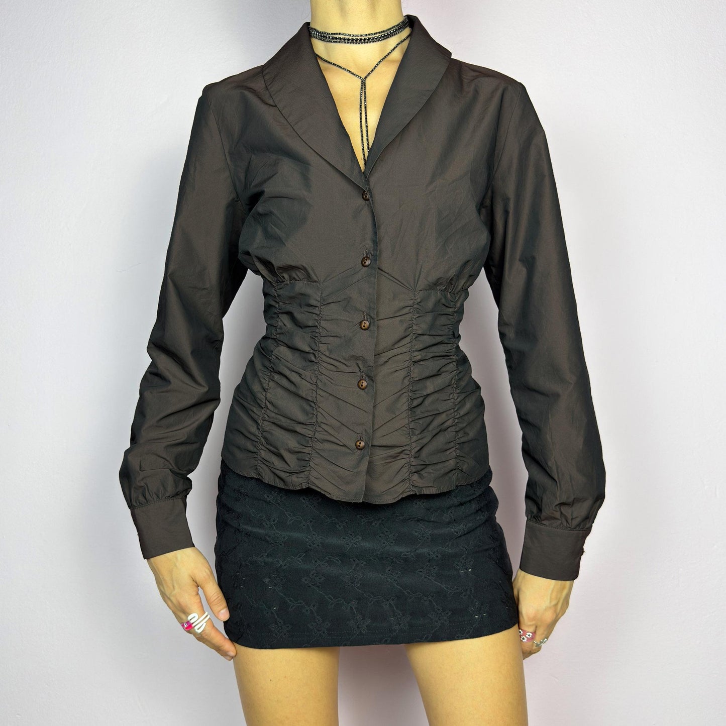 The Vintage 90s Brown Ruched Blouse features a structured yet feminine design with ruched detailing on both the front and back, creating a flattering silhouette. Crafted in a deep brown tone, it includes a tailored collar. adult world shop