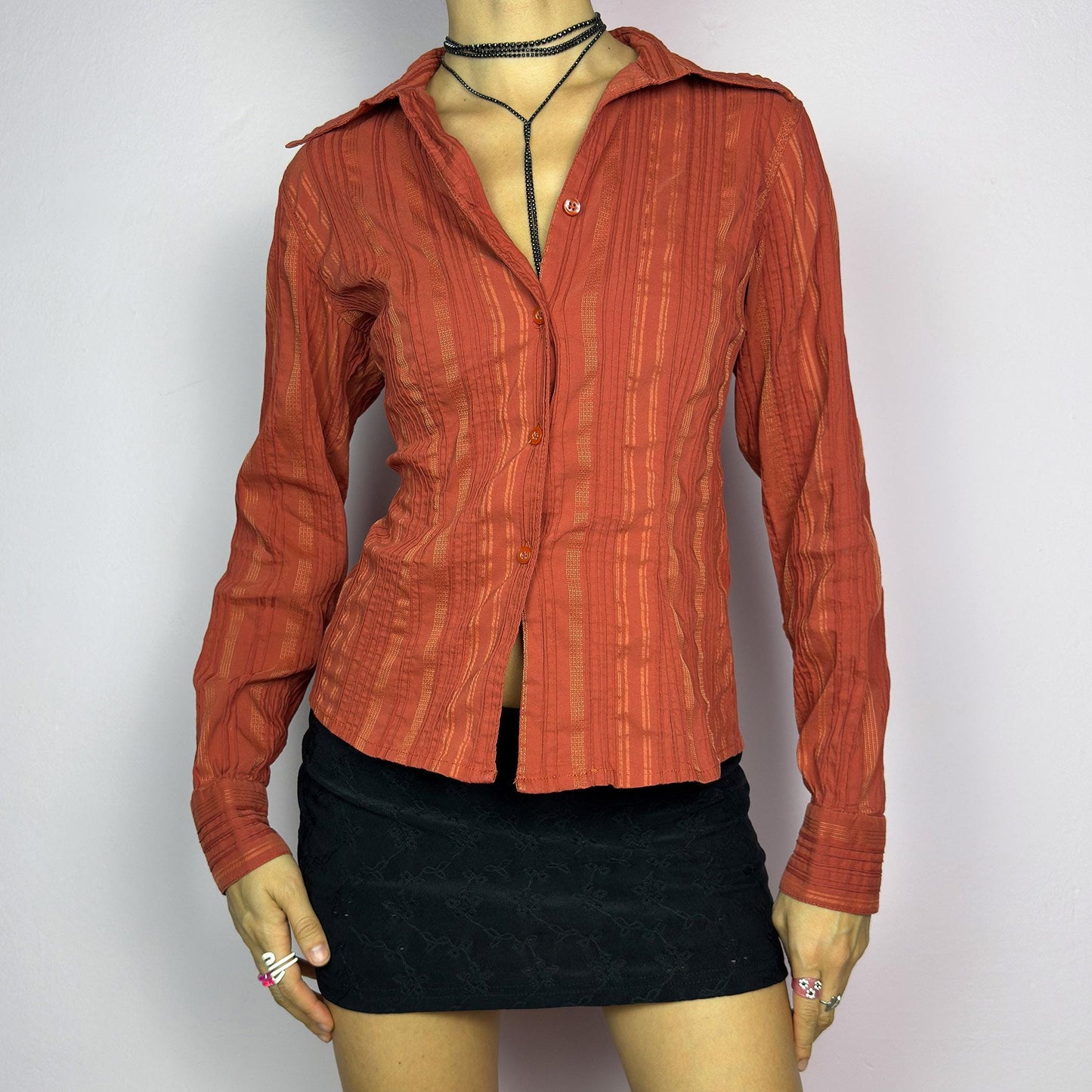 The Y2K Orange Striped Blouse is a vintage 2000s shirt featuring a warm rust-orange hue with a subtle striped pattern, a flattering tailored fit, and a hint of stretch. This long-sleeve button-up blouse is perfect for office wear. adult world shop
