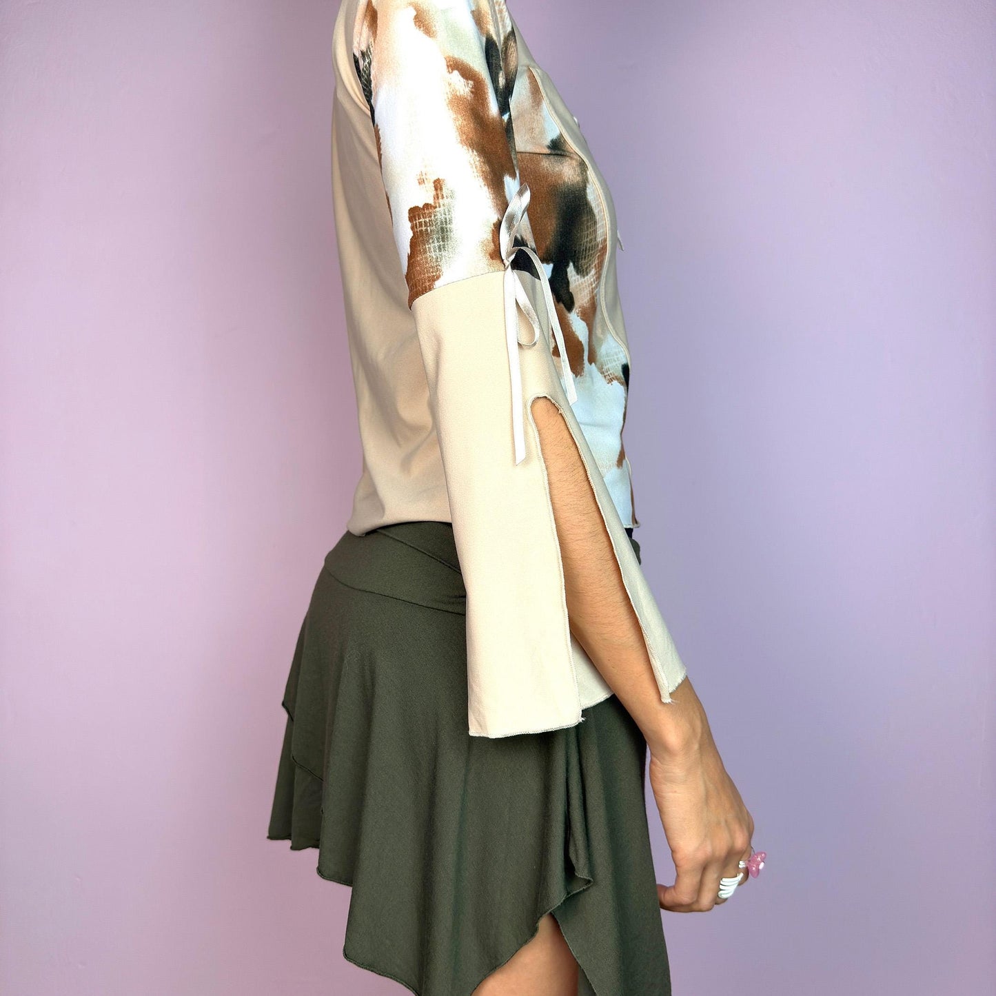 The Y2K Beige Bell Sleeve Top is a vintage 2000s blouse crafted from a stretchy fabric and featuring an abstract print on the sleeves and side panels, contrasted with a solid beige bodice. The design includes a lace-up front detail. adult world shop