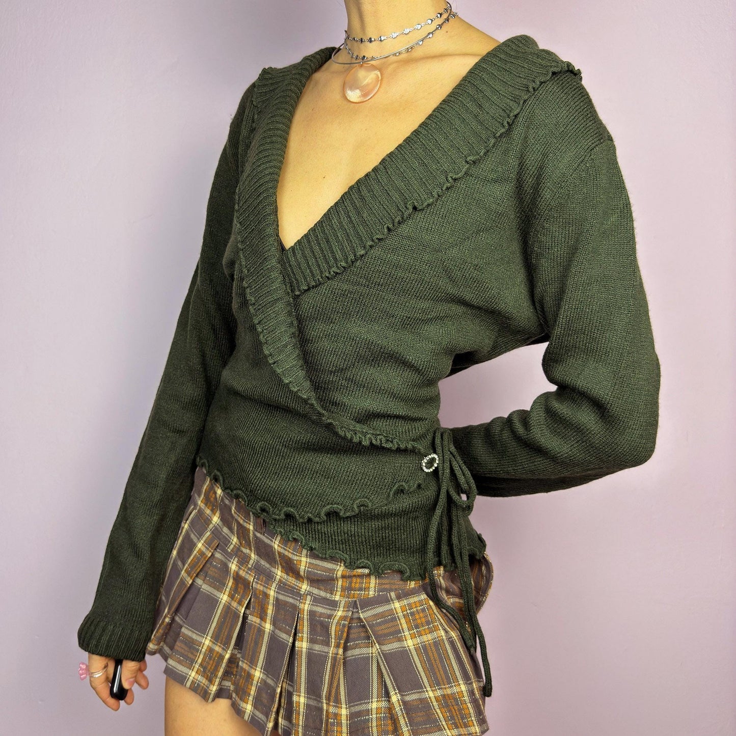 The Y2K Green Wrap Tie Cardigan is a vintage 2000s piece, featuring a deep V-neck, wrap-front design with tie closure, and subtle ruffle details along the neckline. Made from a soft mohair and acrylic blend, this cardigan has a rich forest green tone, perfect for layering over casual or dressed-up outfits. adult world shop