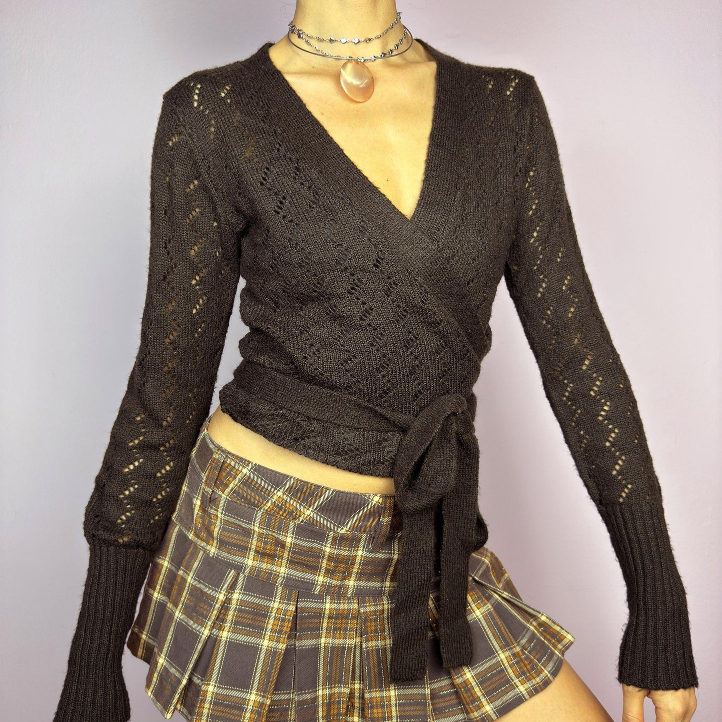 The Y2K Brown Wrap Tie Cardigan is a vintage 2000s piece, featuring a deep V-neckline, delicate open-knit details, and a wrap-around tie closure that cinches at the waist. Crafted from a soft and stretchy knit in a rich chocolate brown shade, this cardigan is perfect for layering over casual and dressy outfits. adult world shop