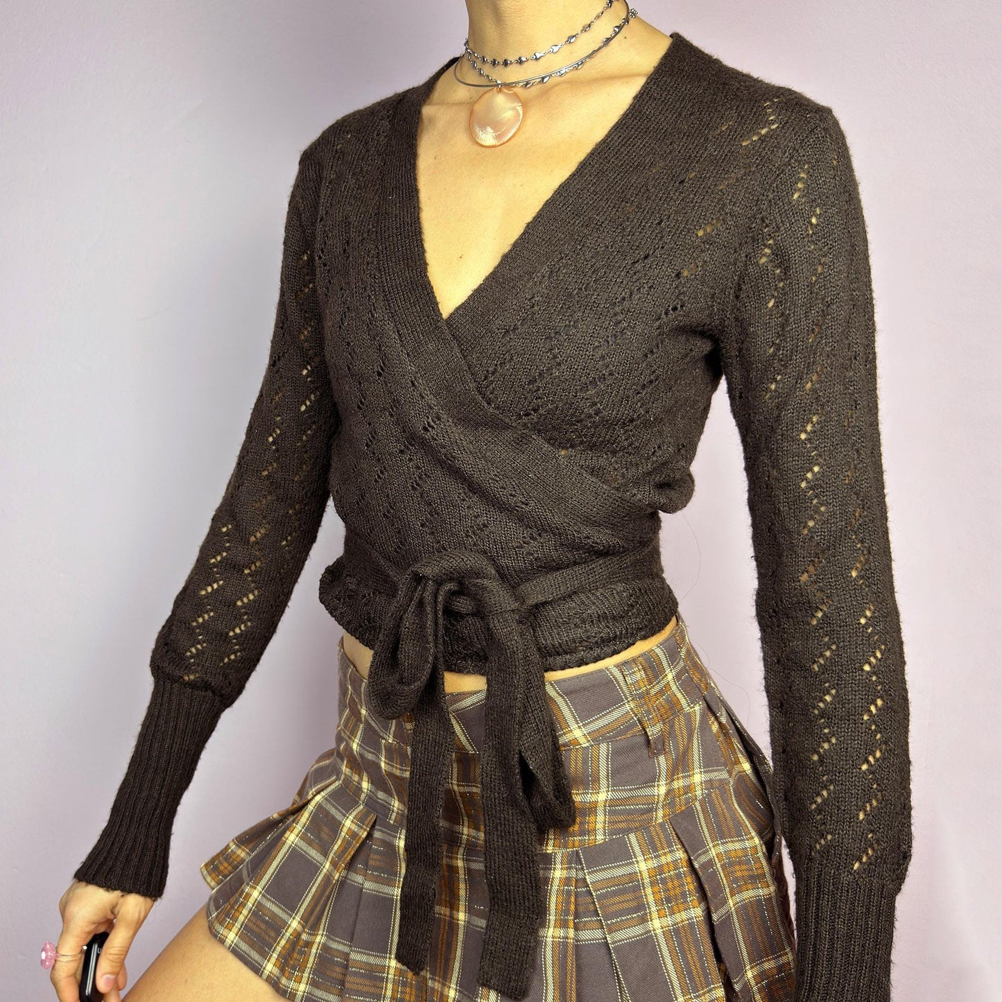 The Y2K Brown Wrap Tie Cardigan is a vintage 2000s piece, featuring a deep V-neckline, delicate open-knit details, and a wrap-around tie closure that cinches at the waist. Crafted from a soft and stretchy knit in a rich chocolate brown shade, this cardigan is perfect for layering over casual and dressy outfits. adult world shop