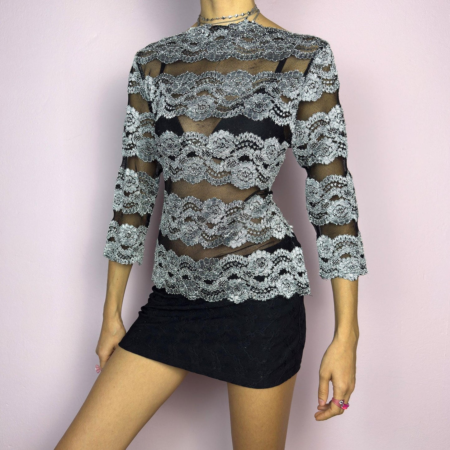 The Y2K Lace Mesh Black Top is a vintage 2000s statement sheer blouse featuring a delicate black mesh base with intricate silver lace embroidery in horizontal stripes. Designed with a fitted silhouette and three-quarter sleeves, this top is perfect for a romantic night or a bold evening outfit.