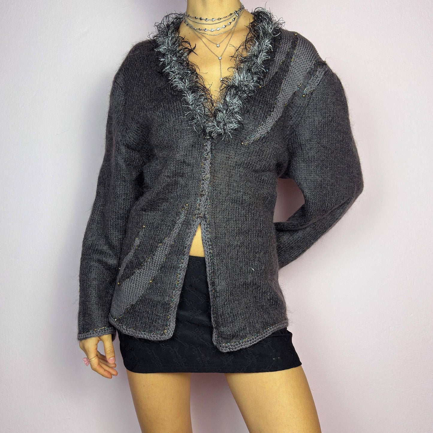 The Vintage 90s Gray Shaggy Trim Cardigan is a unique statement knitwear piece, featuring a soft knit fabric. Designed with a shaggy, hairy-textured trim along the V-neckline, subtle beaded embellishments, and button closure, this cardigan is perfect for cozy winter outfits. adult world shop