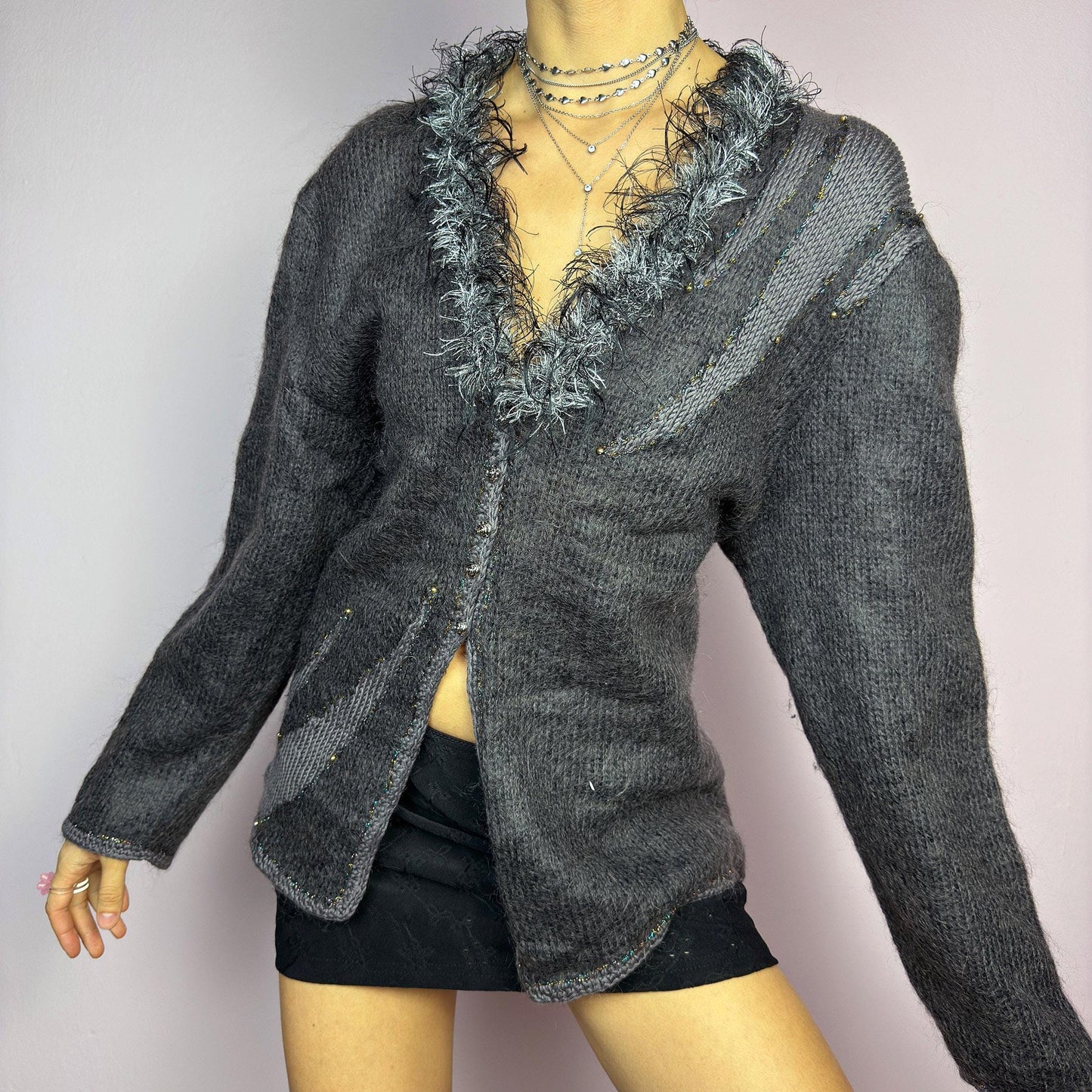 The Vintage 90s Gray Shaggy Trim Cardigan is a unique statement knitwear piece, featuring a soft knit fabric. Designed with a shaggy, hairy-textured trim along the V-neckline, subtle beaded embellishments, and button closure, this cardigan is perfect for cozy winter outfits. adult world shop