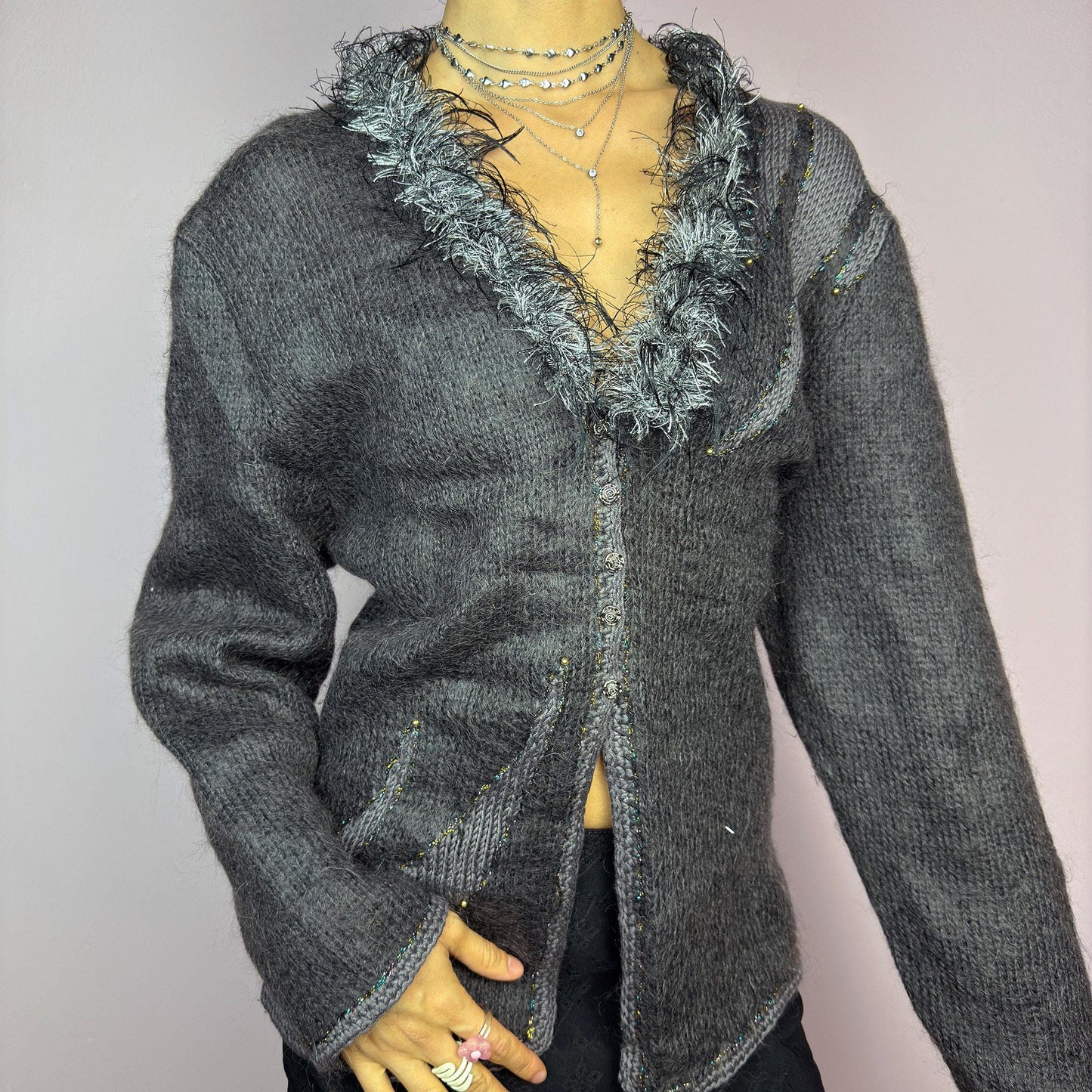 The Vintage 90s Gray Shaggy Trim Cardigan is a unique statement knitwear piece, featuring a soft knit fabric. Designed with a shaggy, hairy-textured trim along the V-neckline, subtle beaded embellishments, and button closure, this cardigan is perfect for cozy winter outfits. adult world shop