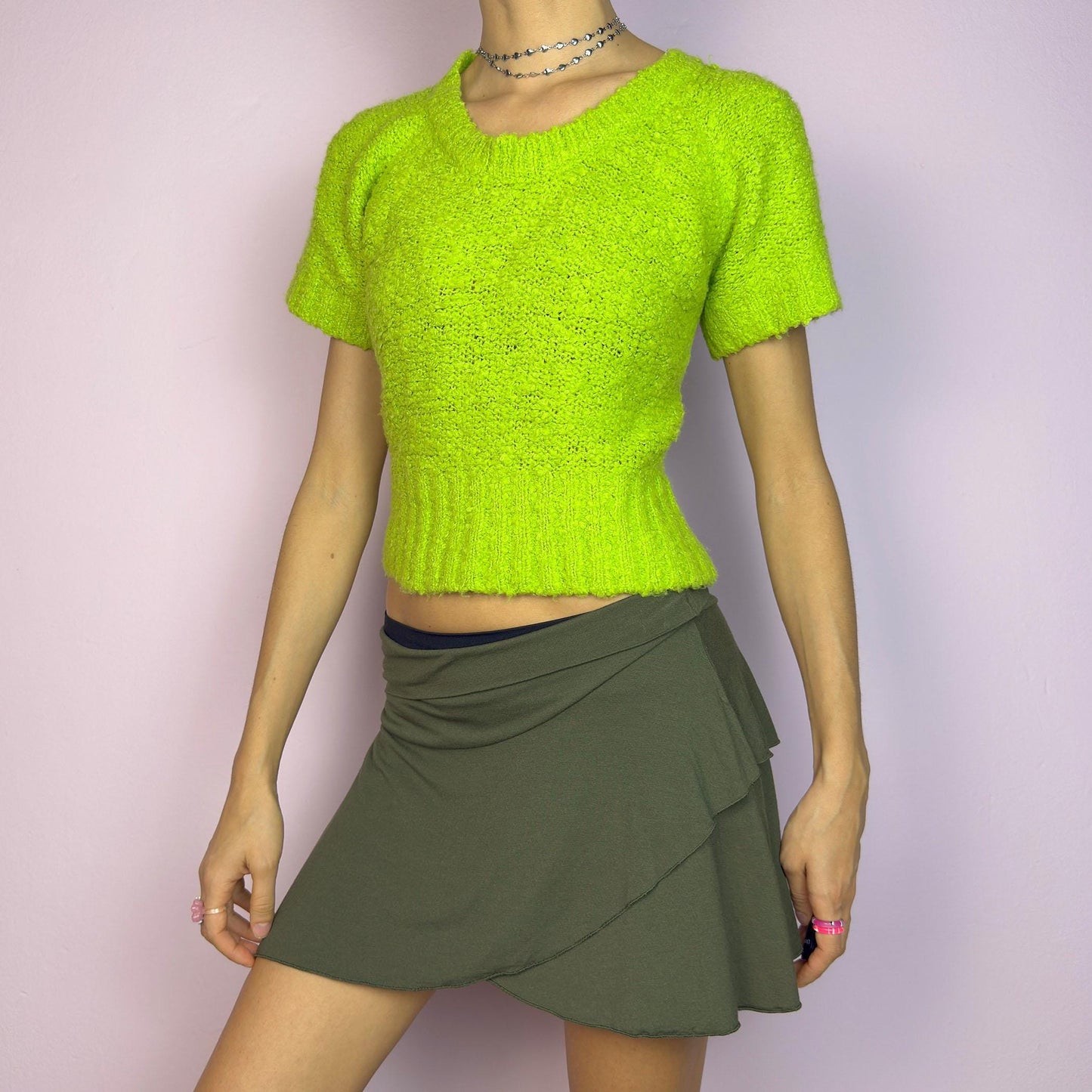 The Y2K Green Knitted Top is a vibrant vintage 2000s piece featuring a lime-green hue. Designed with a cropped silhouette, short sleeves, and a stretchy ribbed hem, this knit top adds a playful touch to casual outfits. adult world shop