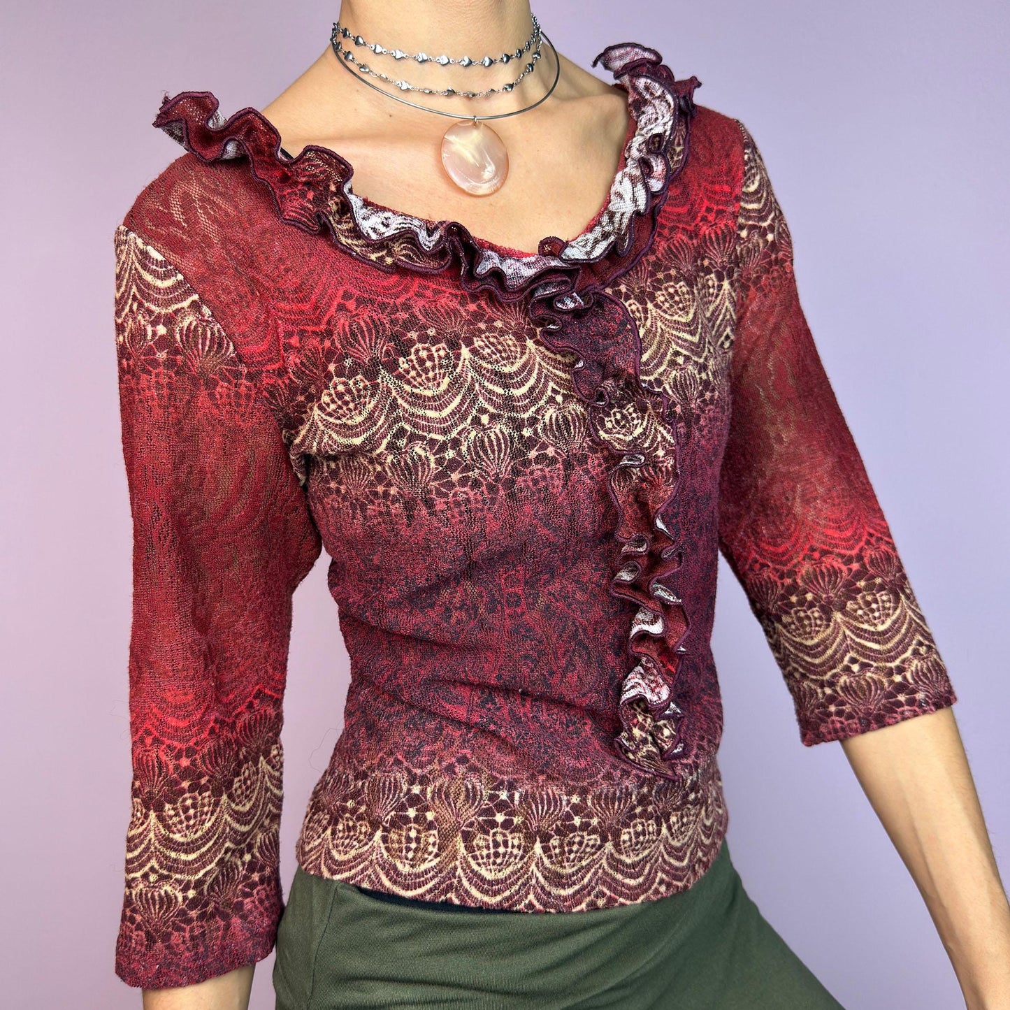 The Y2K Maroon Ruffle Mesh Top is a romantic vintage 2000s piece. Featuring a semi-sheer lace-inspired design in warm red tones, it showcases intricate patterns complemented by a ruffled neckline and 3/4 sleeves. adult world shop