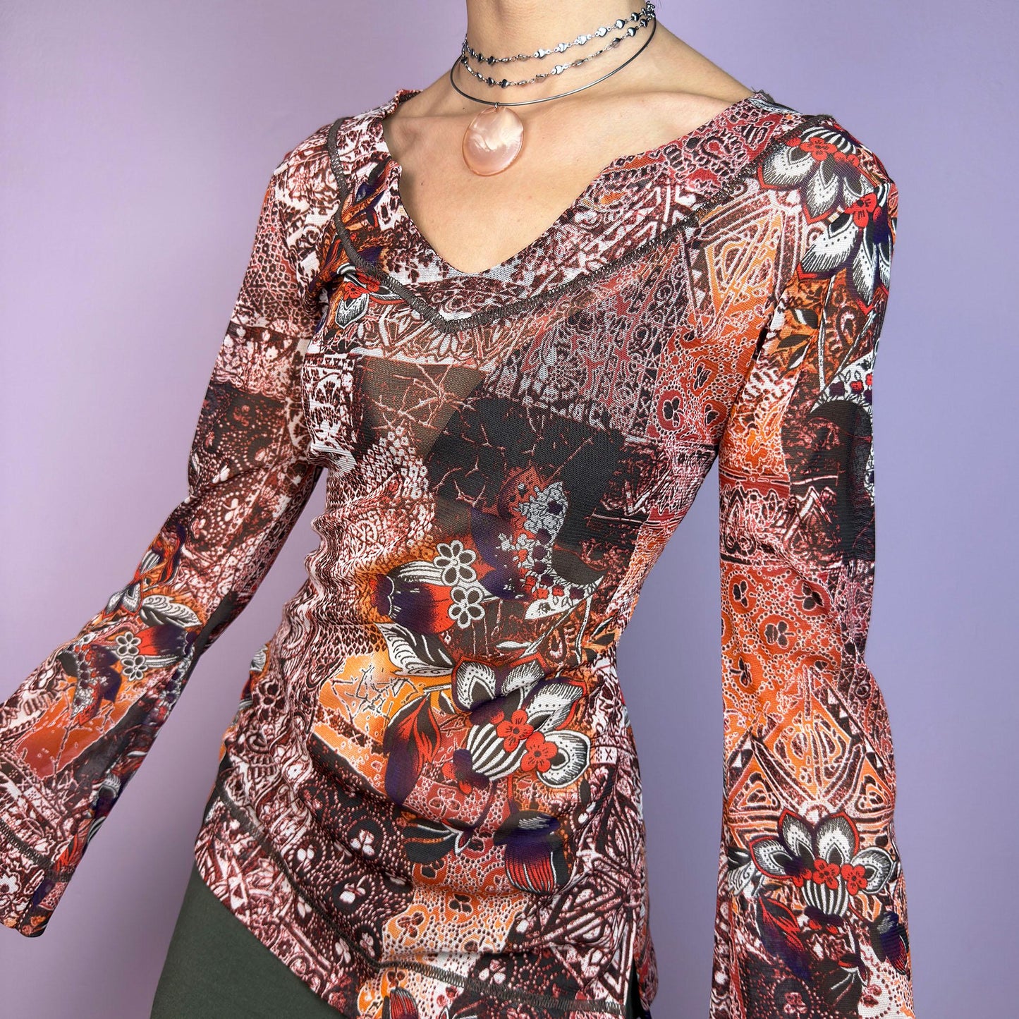 The Y2K Mesh Flared Long Sleeve Top is a vibrant vintage 2000s piece, featuring a floral and paisley print in earthy tones of orange, red, and brown. Crafted from lightweight mesh fabric, this top has a semi-sheer finish. adult world shop