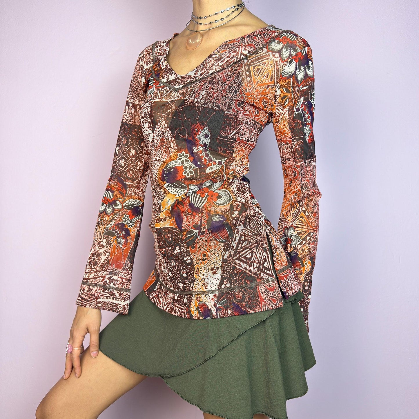 The Y2K Mesh Flared Long Sleeve Top is a vibrant vintage 2000s piece, featuring a floral and paisley print in earthy tones of orange, red, and brown. Crafted from lightweight mesh fabric, this top has a semi-sheer finish. adult world shop