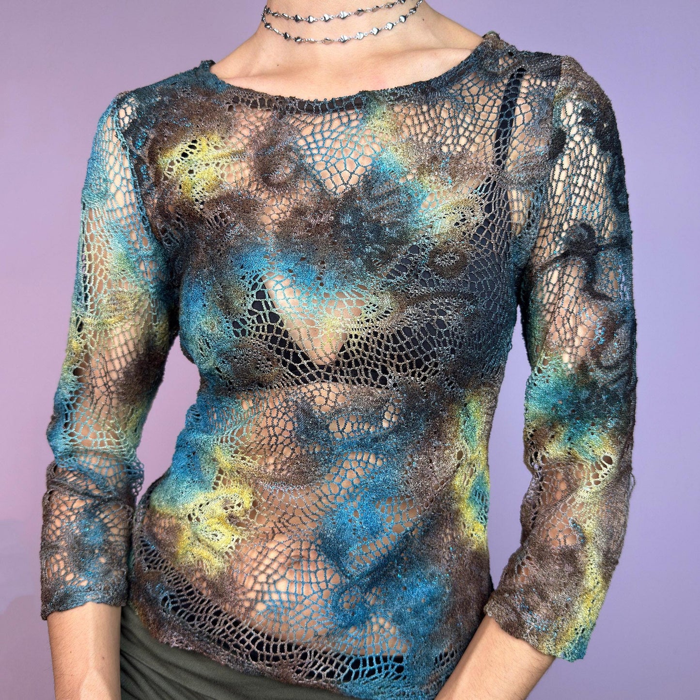 The Y2K Open Knit Mesh Top is a unique vintage 2000s piece featuring an intricate open-knit design, this semi-sheer top boasts a dreamy tie-dye-inspired blend of earthy hues in brown, blue and green. adult world shop