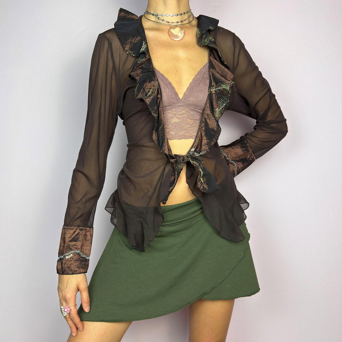 The Y2K Brown Mesh Tie Front Top is a vintage 2000s elegant and flirty piece. This semi-sheer mesh blouse features a tie-front closure and a cascade of ruffle detailing along the neckline and cuffs. adult world shop