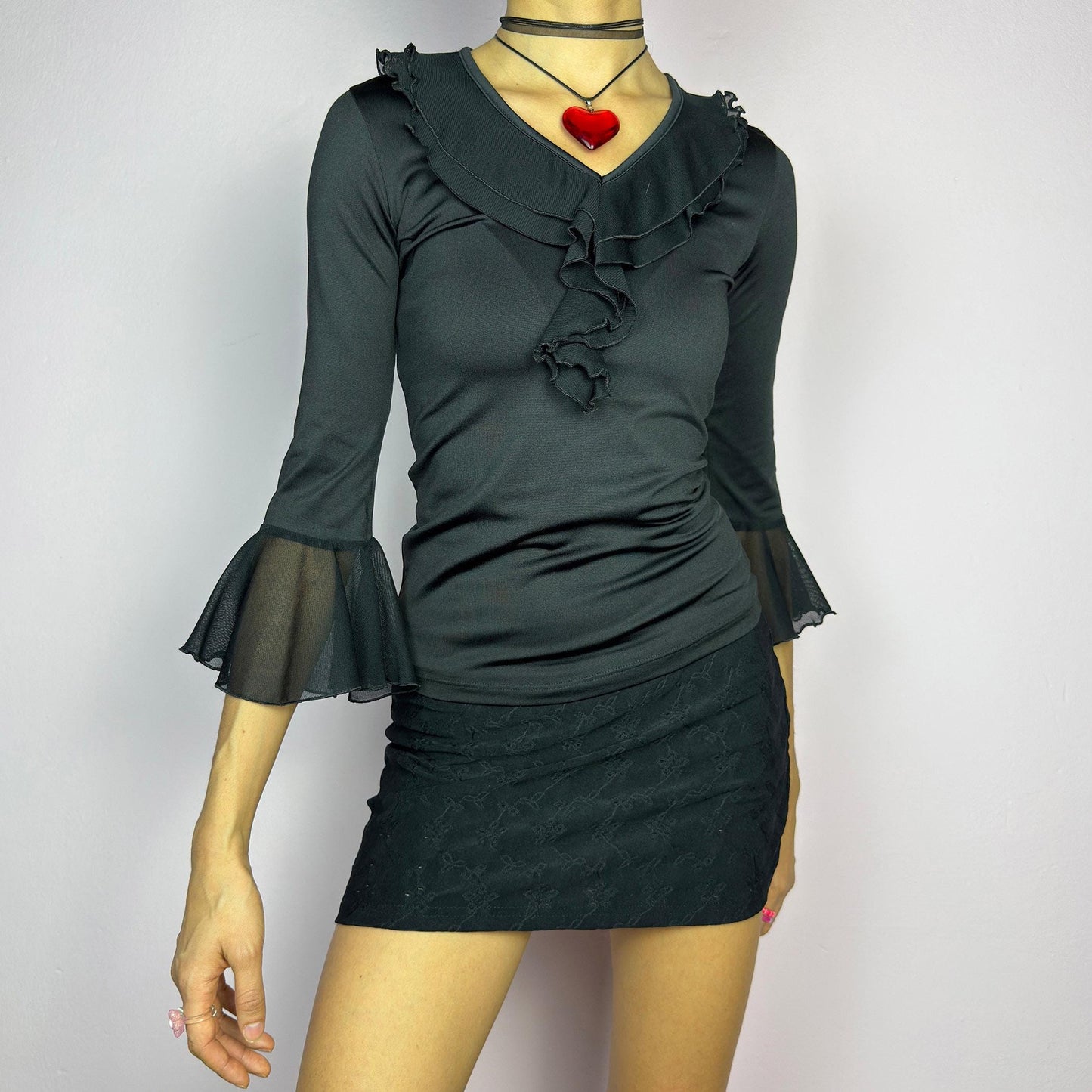 The Y2K Black Ruffle Bell Sleeve Top is a sleek and elegant vintage 2000s piece. Featuring a fitted silhouette with cascading ruffles along the neckline and a flattering V-neck design. The three-quarter bell sleeves with sheer mesh. adult world shop