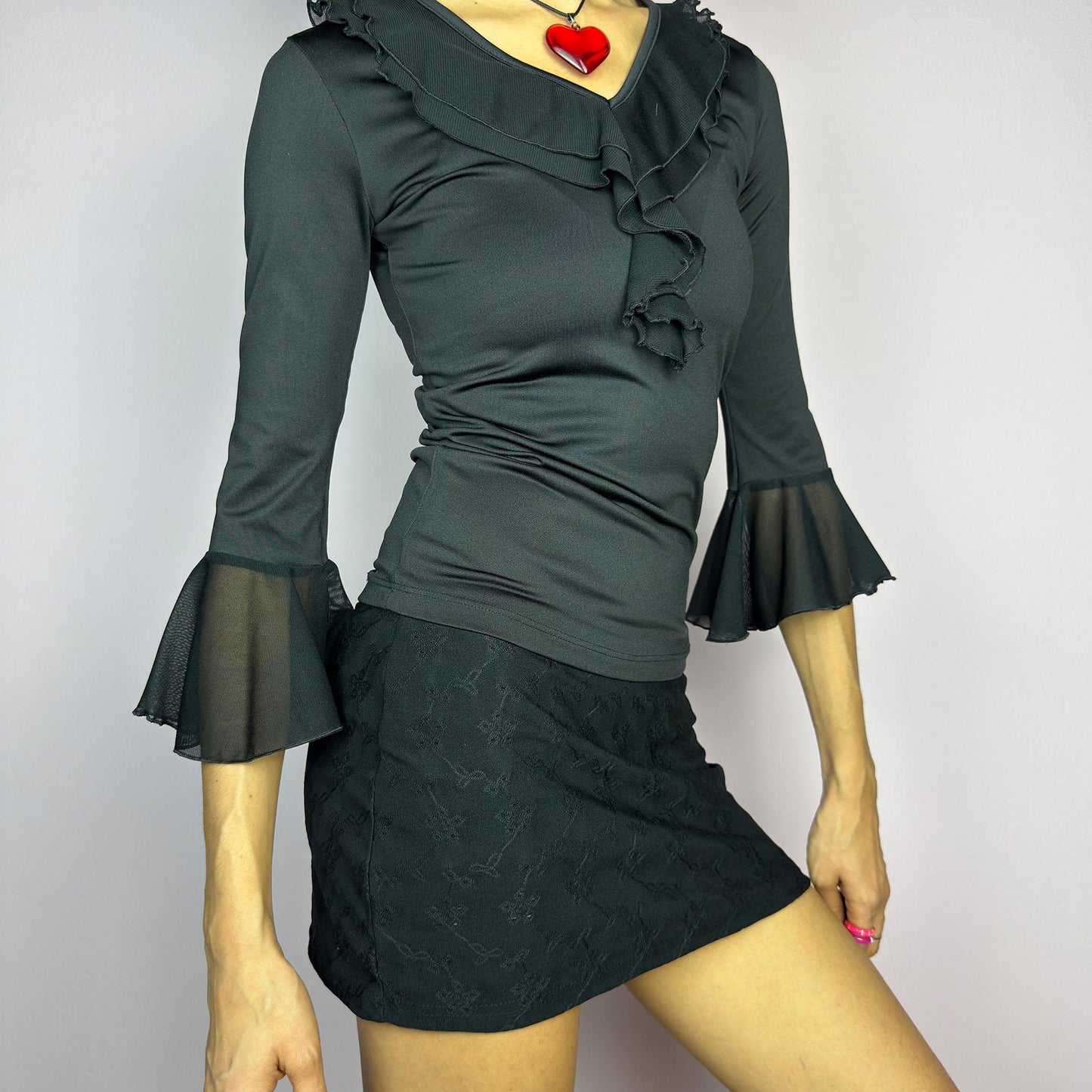 The Y2K Black Ruffle Bell Sleeve Top is a sleek and elegant vintage 2000s piece. Featuring a fitted silhouette with cascading ruffles along the neckline and a flattering V-neck design. The three-quarter bell sleeves with sheer mesh. adult world shop