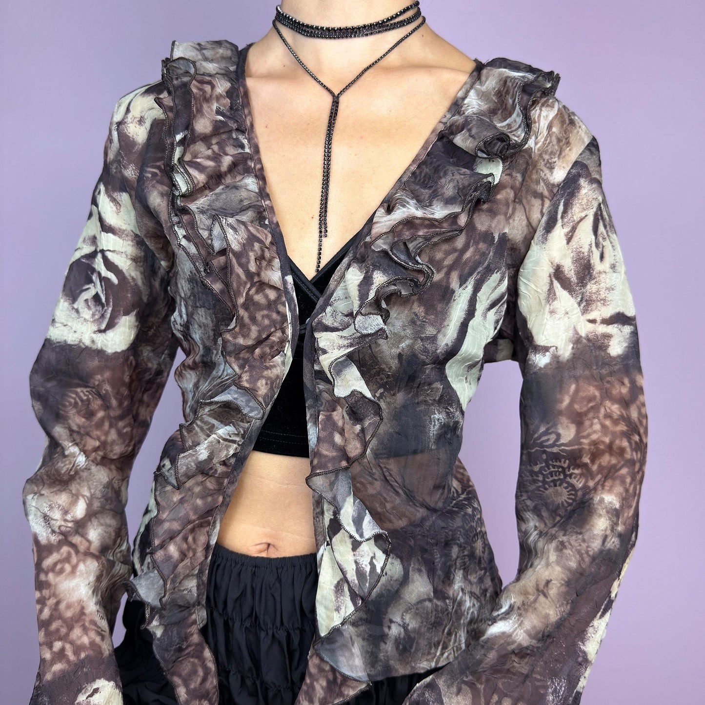 The Y2K Printed Ruffle Blouse is a stunning vintage 2000s romantic piece crafted from sheer, lightweight fabric in brown tones and featuring a blend of earthy hues in a rose-patterned print. adult world shop