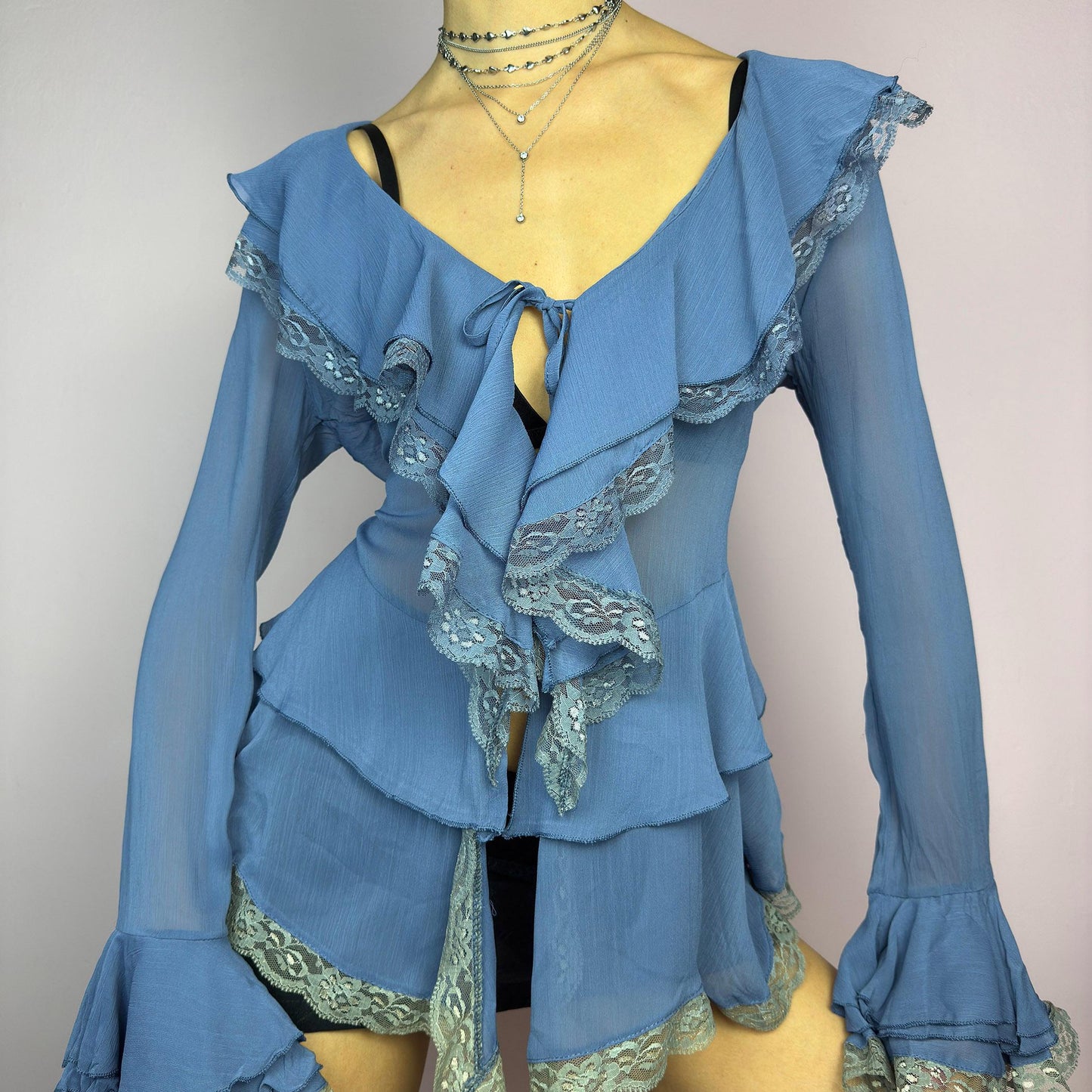 The Y2K Blue Ruffle Blouse is a dreamy vintage 2000s piece with a romantic and ethereal aesthetic. Crafted from a sheer, lightweight fabric in a soft blue shade, this blouse features cascading ruffles with delicate lace trim. adult world shop