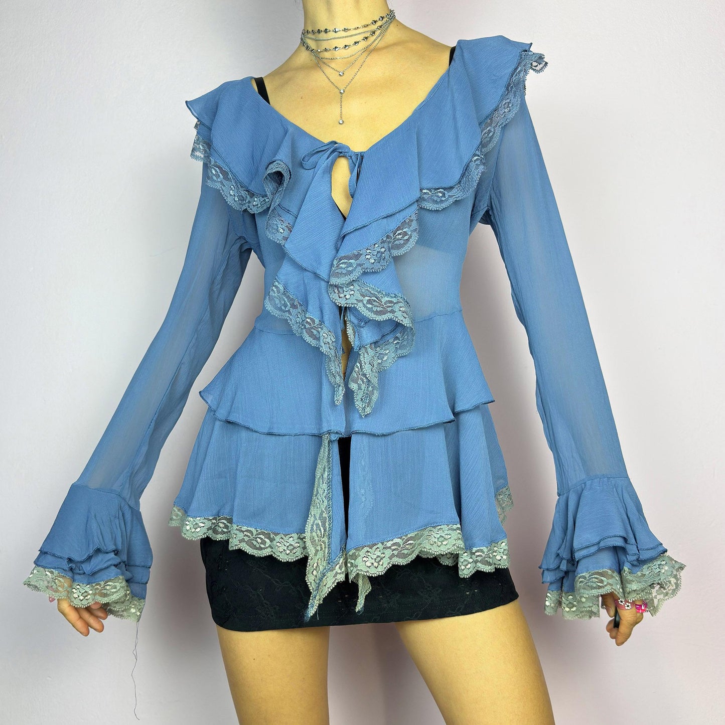 The Y2K Blue Ruffle Blouse is a dreamy vintage 2000s piece with a romantic and ethereal aesthetic. Crafted from a sheer, lightweight fabric in a soft blue shade, this blouse features cascading ruffles with delicate lace trim. adult world shop