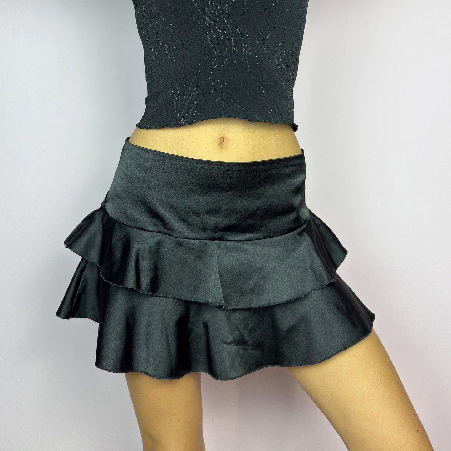 The Y2K Black Ruffle Satin Mini Skirt is a vintage 2000s piece made from a sleek satin-style stretchy fabric featuring layered ruffles, low rise design and a side zipper closure. Ideal for a night-out outfit. adult world shop