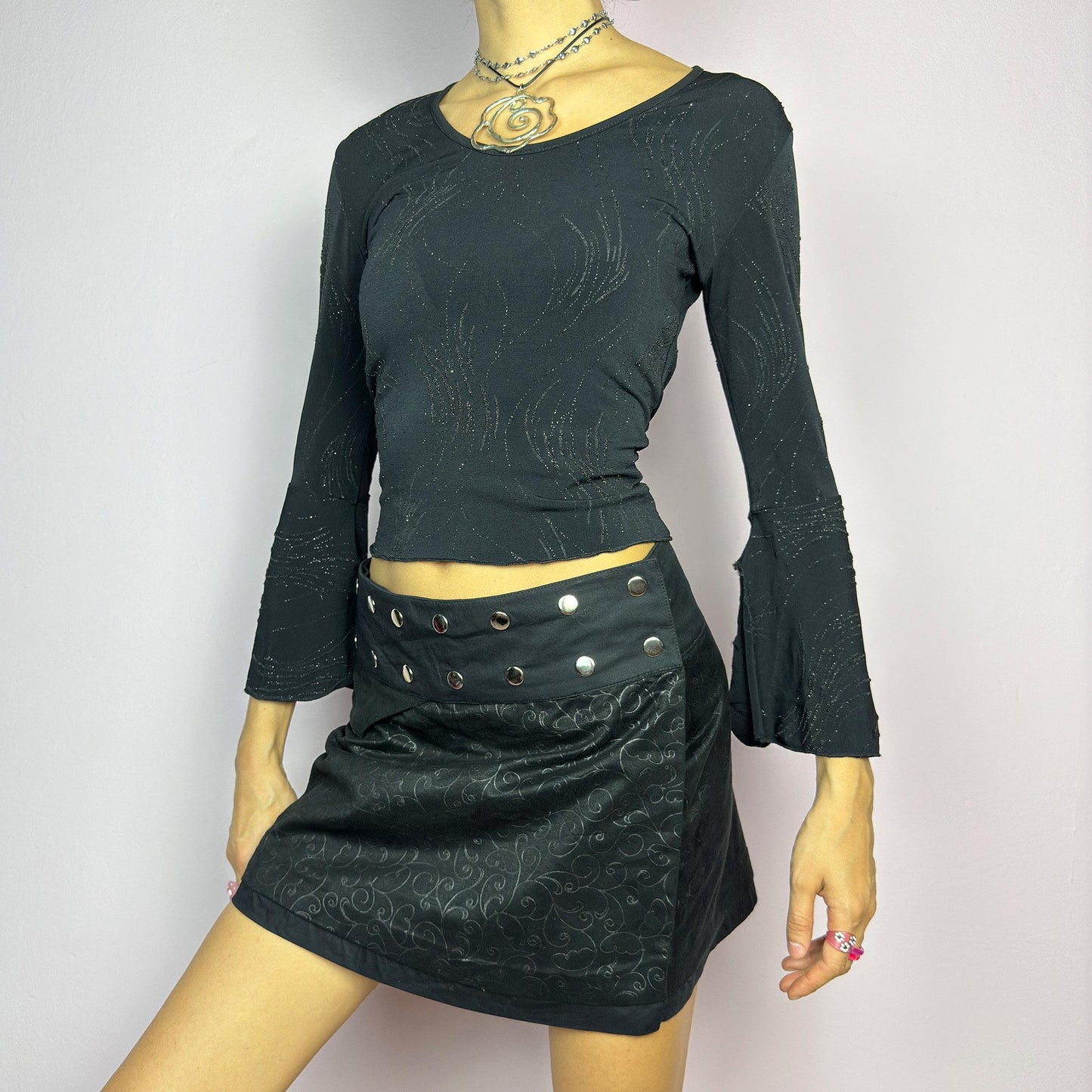 The Y2K Wrap Mini Black Skirt is a vintage 2000s piece featuring a snap-button closure on the waistband for an adjustable fit. Made from a thick fabric with a subtle floral pattern design, its wrap silhouette. adult world shop