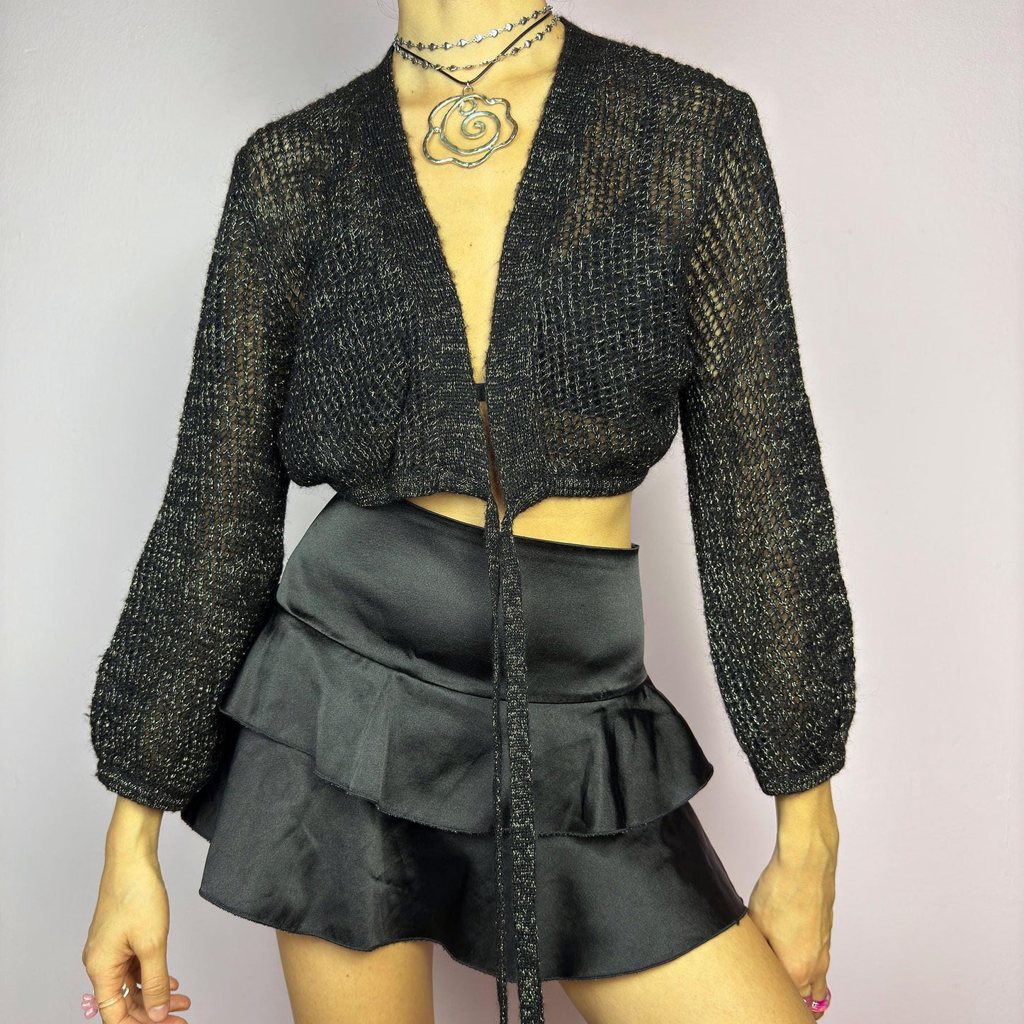 This Y2K Black Tie Front Cardigan is a vintage 2000s piece featuring a lightweight open-knit design with a subtle metallic shimmer, a cropped fit and long sleeves. Perfect for layering and ideal for night-out or casual outfits.