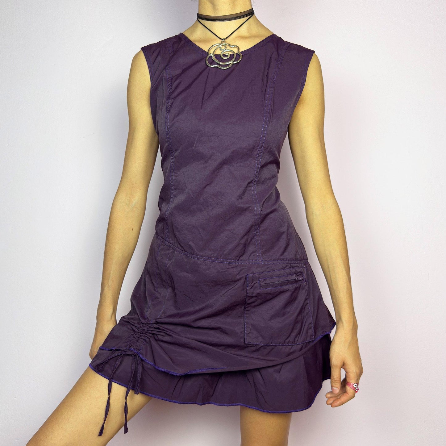 The Y2K Purple Layered Mini Dress is a vintage 2000s sleeveless dress in a deep purple hue, featuring a structured, layered silhouette, a side pocket, an adjustable drawstring ruched detail on the side for a customizable fit. adult world shop
