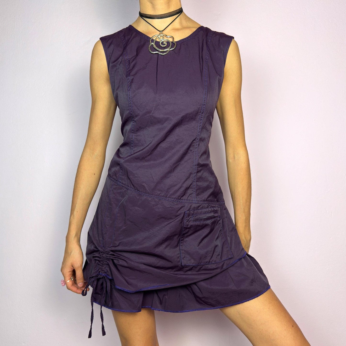 The Y2K Purple Layered Mini Dress is a vintage 2000s sleeveless dress in a deep purple hue, featuring a structured, layered silhouette, a side pocket, an adjustable drawstring ruched detail on the side for a customizable fit. adult world shop