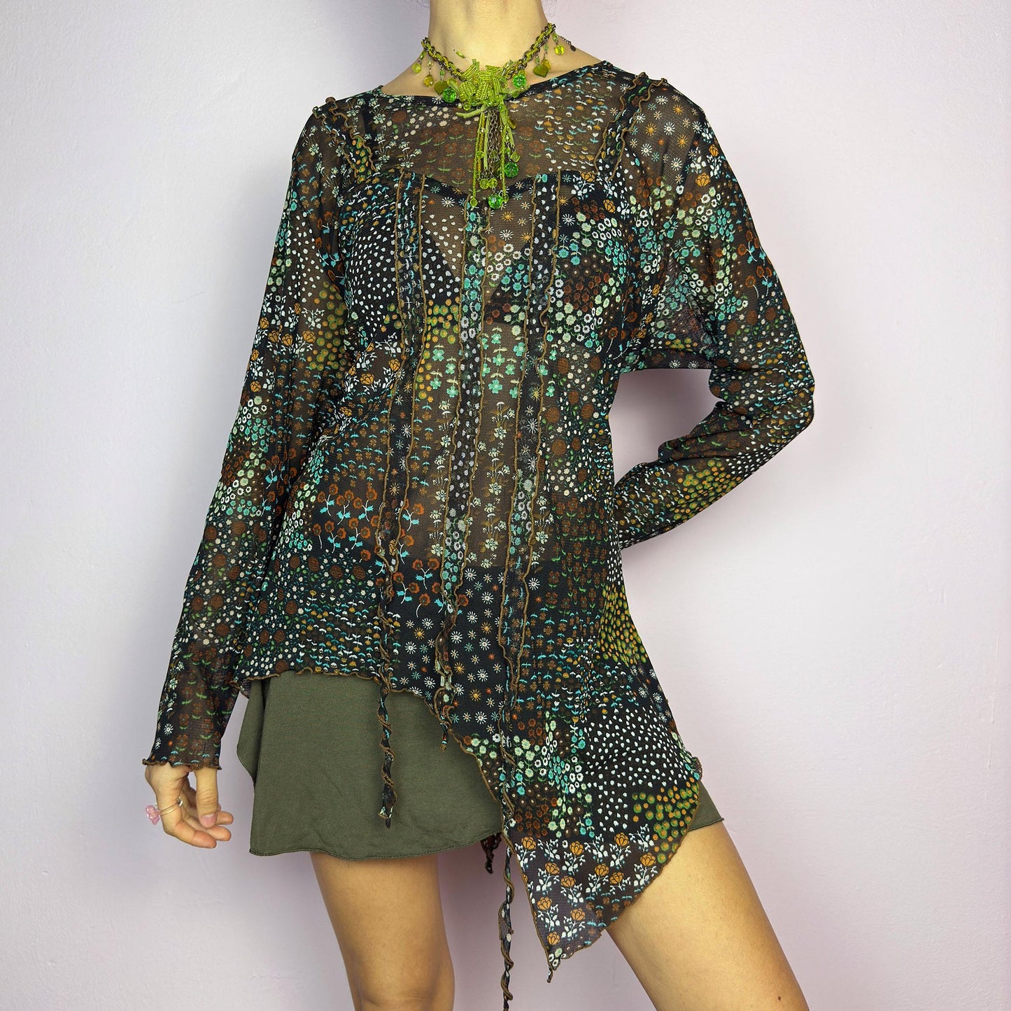 The Y2K Black Asymmetric Mesh Top is a vintage 2000s statement piece featuring semi-sheer mesh fabric with a floral and geometric print. Designed with an edgy asymmetric cut and delicate lettuce hem detailing, this top embodies a deconstructed aesthetic with a fairy grunge-inspired touch. The lightweight, stretchy fabric makes it perfect for layering, making it an ideal choice for summer avant-garde outfits. adult world shop