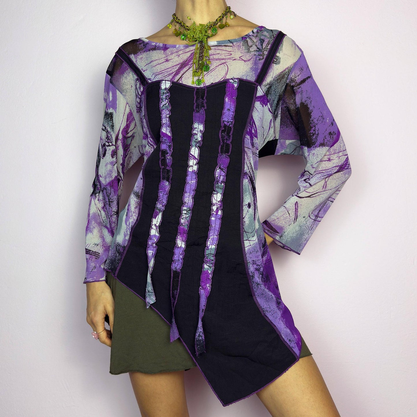 The Y2K Mesh Asymmetric Black Top is a vintage 2000s piece featuring a semi-sheer mesh fabric with an abstract purple, black, and white print. Designed with three quarter sleeves and contrast paneling and exposed seams, this top has a deconstructed, edgy aesthetic. The asymmetric hem and raw cut details add a unique touch, making it perfect for grunge or fairycore-inspired outfits. Lightweight and stretchy, ideal for layering and statement looks. adult world shop