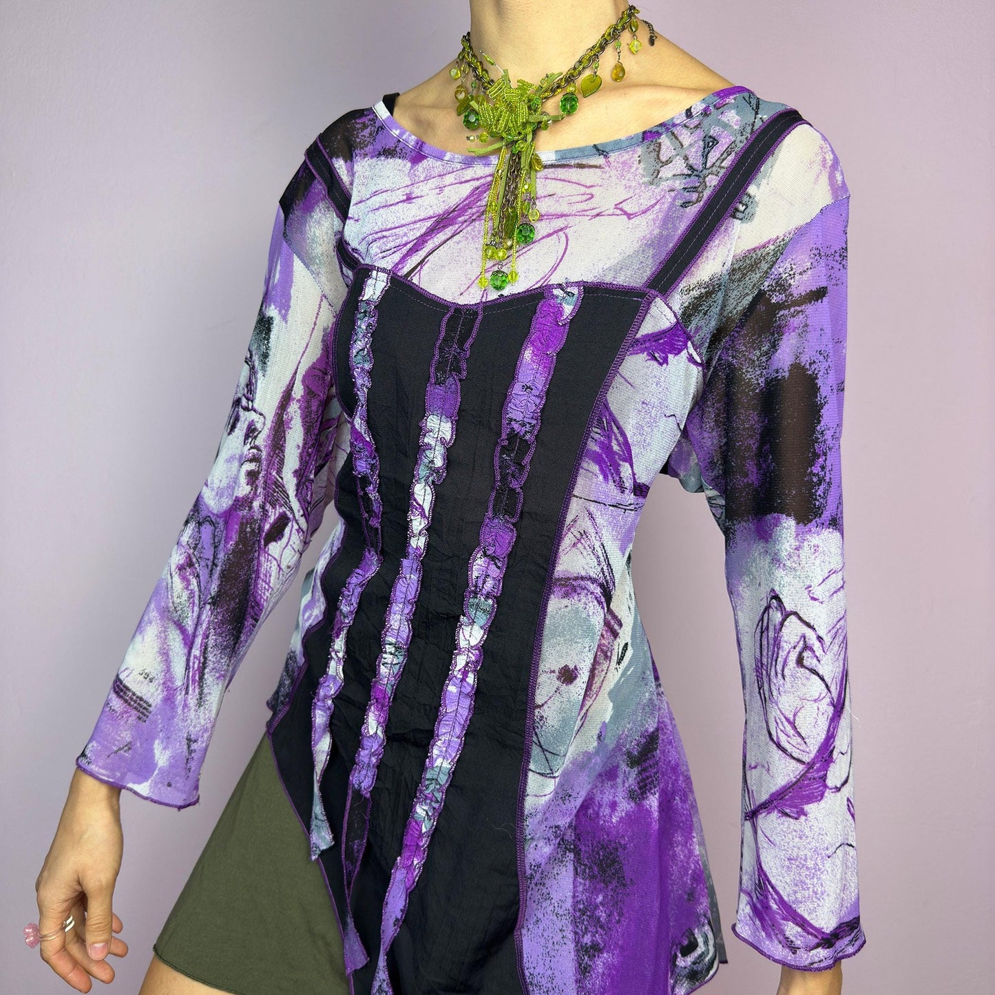 The Y2K Mesh Asymmetric Black Top is a vintage 2000s piece featuring a semi-sheer mesh fabric with an abstract purple, black, and white print. Designed with three quarter sleeves and contrast paneling and exposed seams, this top has a deconstructed, edgy aesthetic. The asymmetric hem and raw cut details add a unique touch, making it perfect for grunge or fairycore-inspired outfits. Lightweight and stretchy, ideal for layering and statement looks. adult world shop