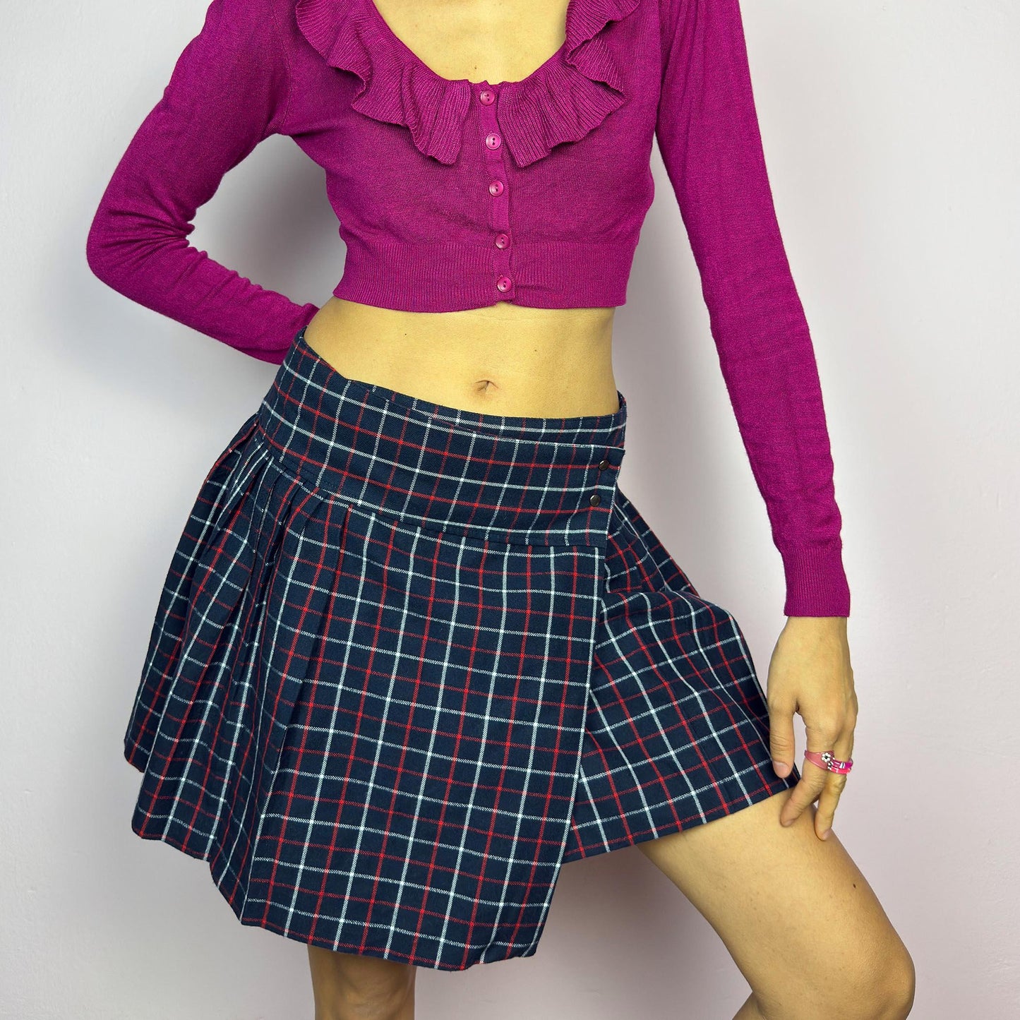 The Y2K Plaid Pleated Wrap Mini Skirt is a vintage 2000s piece featuring a wrap-style waistband with snap button details. Made from a plaid fabric in navy blue tones, it has structured pleats that create a classic silhouette. adult world shop