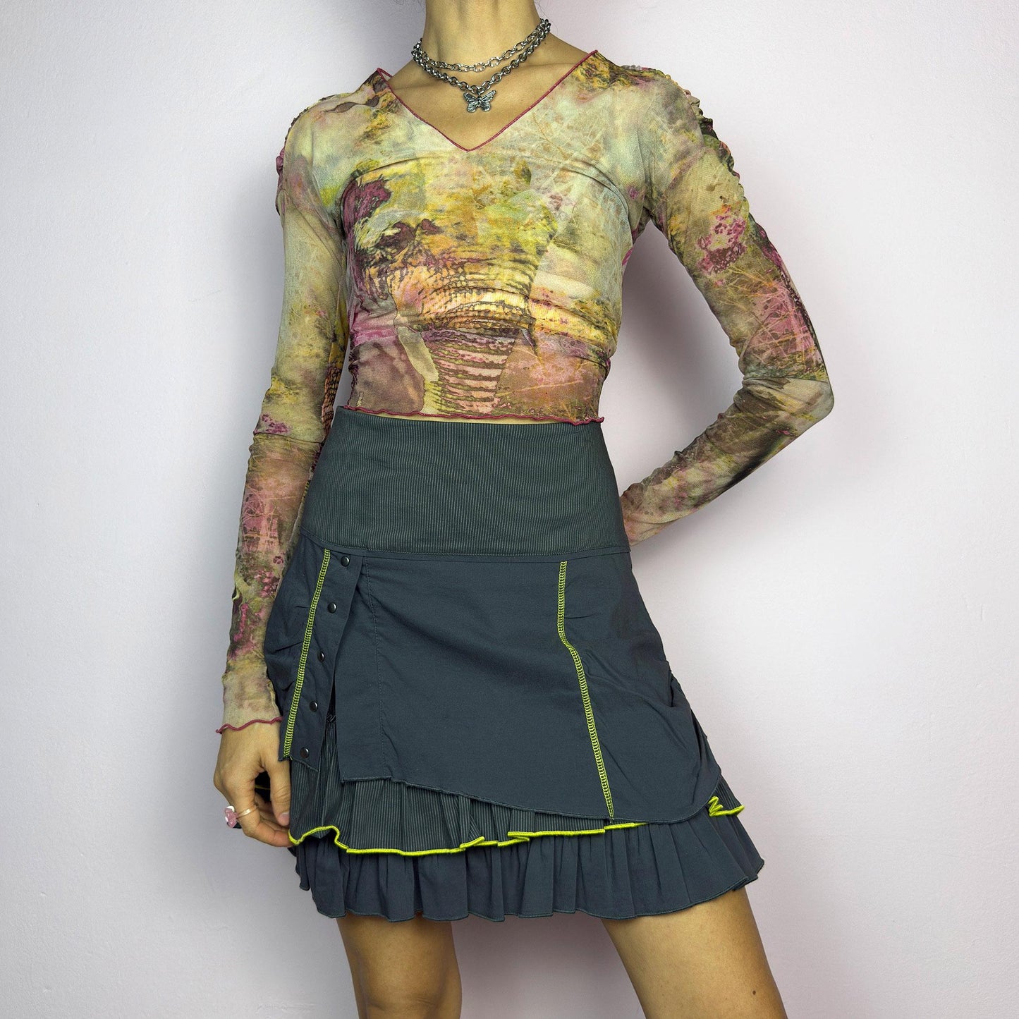 The Y2K Gray Ruffle Mini Skirt is a vintage 2000s statement piece featuring a tiered layered design with yellow contrast stitching details. Designed with a high-waist fit, it includes a side zipper closure. adult world shop