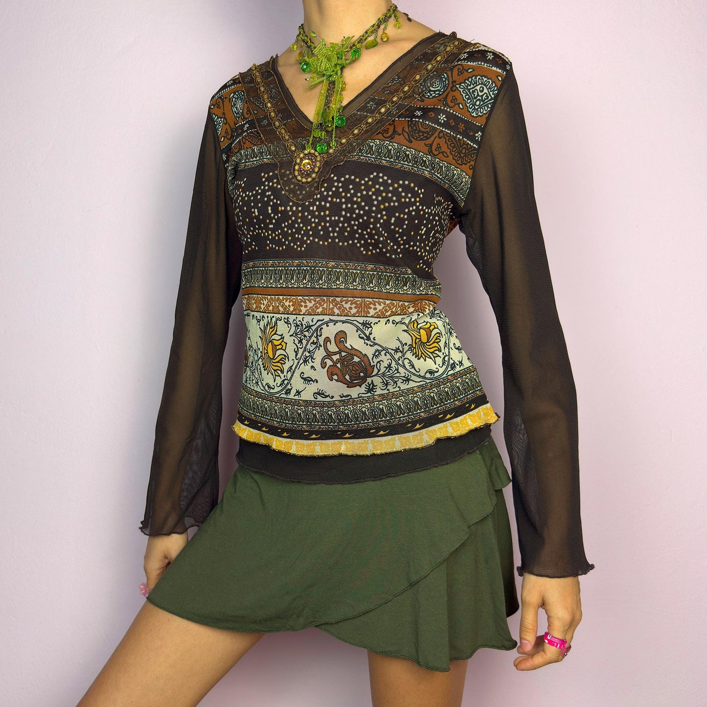 The Y2K Brown Bell Sleeve Mesh Top is a vintage 2000s piece featuring a semi-sheer mesh fabric with baroque and floral-inspired prints. Designed with flared bell sleeves, a fitted silhouette, and a layered hem, this top embodies a dreamy bohemian aesthetic. The lightweight and stretchy fabric make it perfect for ethereal, fairy-grunge looks. adult world shop
