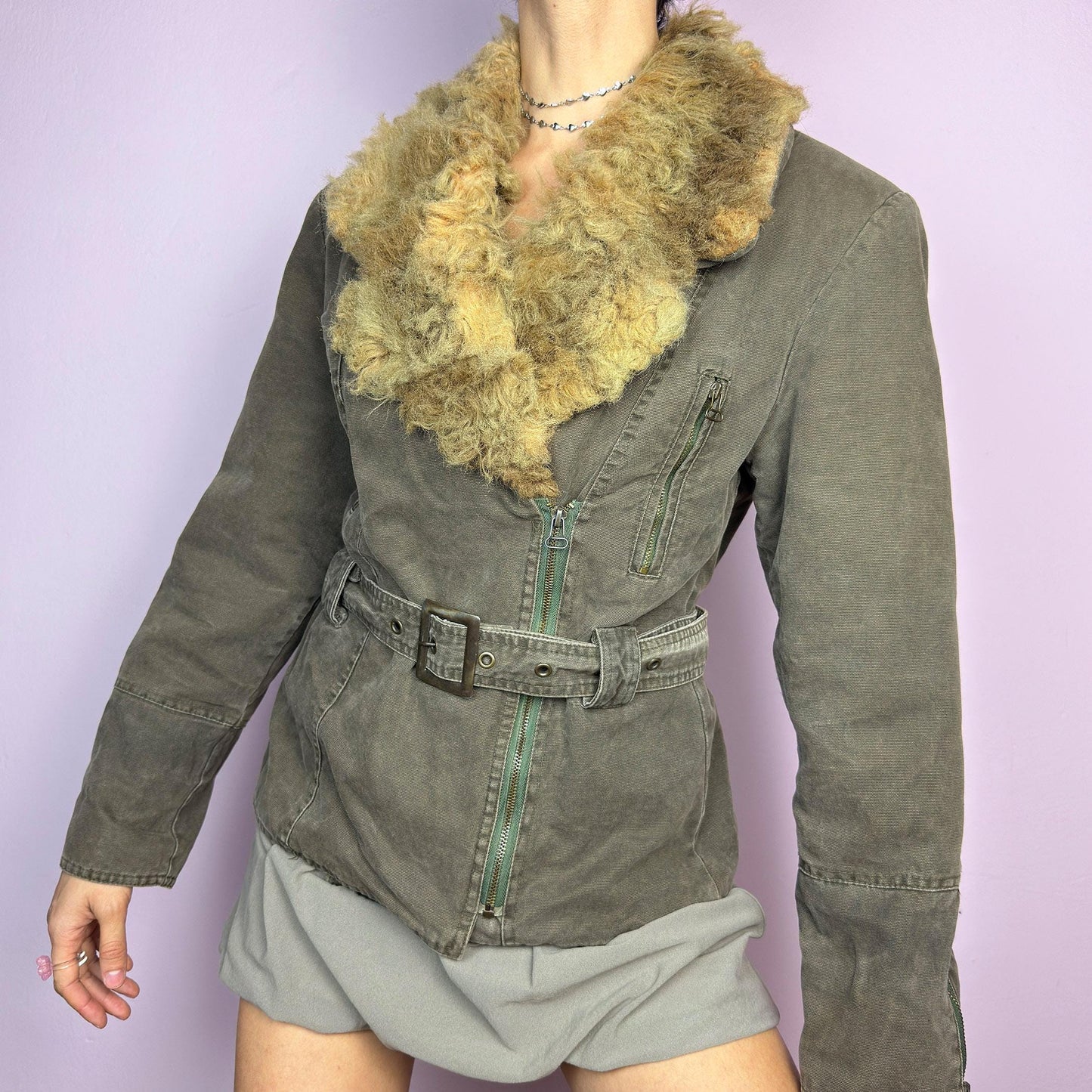 The Y2K Khaki Belted Jacket is a vintage 2000s piece featuring a structured fit with rugged utility-inspired details. Designed with padded shoulders for a strong silhouette, an oversized plush faux-shearling collar, asymmetric zip closure, and an adjustable waist belt for a cinched look. The washed khaki tone and distressed finish add to its edgy, worn-in appeal, making it perfect for grunge or military-inspired winter outfits. A outerwear piece for layering in colder seasons. adult world shop
