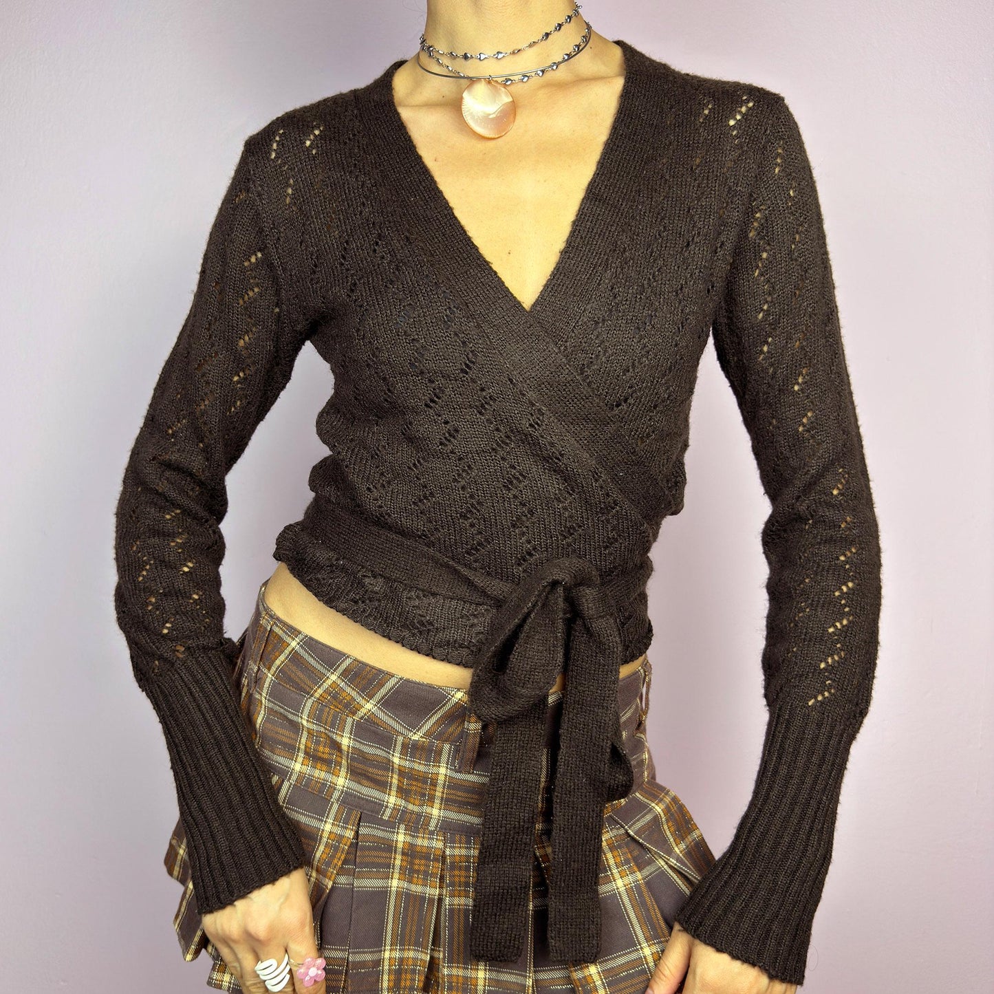 The Y2K Brown Wrap Tie Cardigan is a vintage 2000s piece, featuring a deep V-neckline, delicate open-knit details, and a wrap-around tie closure that cinches at the waist. Crafted from a soft and stretchy knit in a rich chocolate brown shade, this cardigan is perfect for layering over casual and dressy outfits. adult world shop