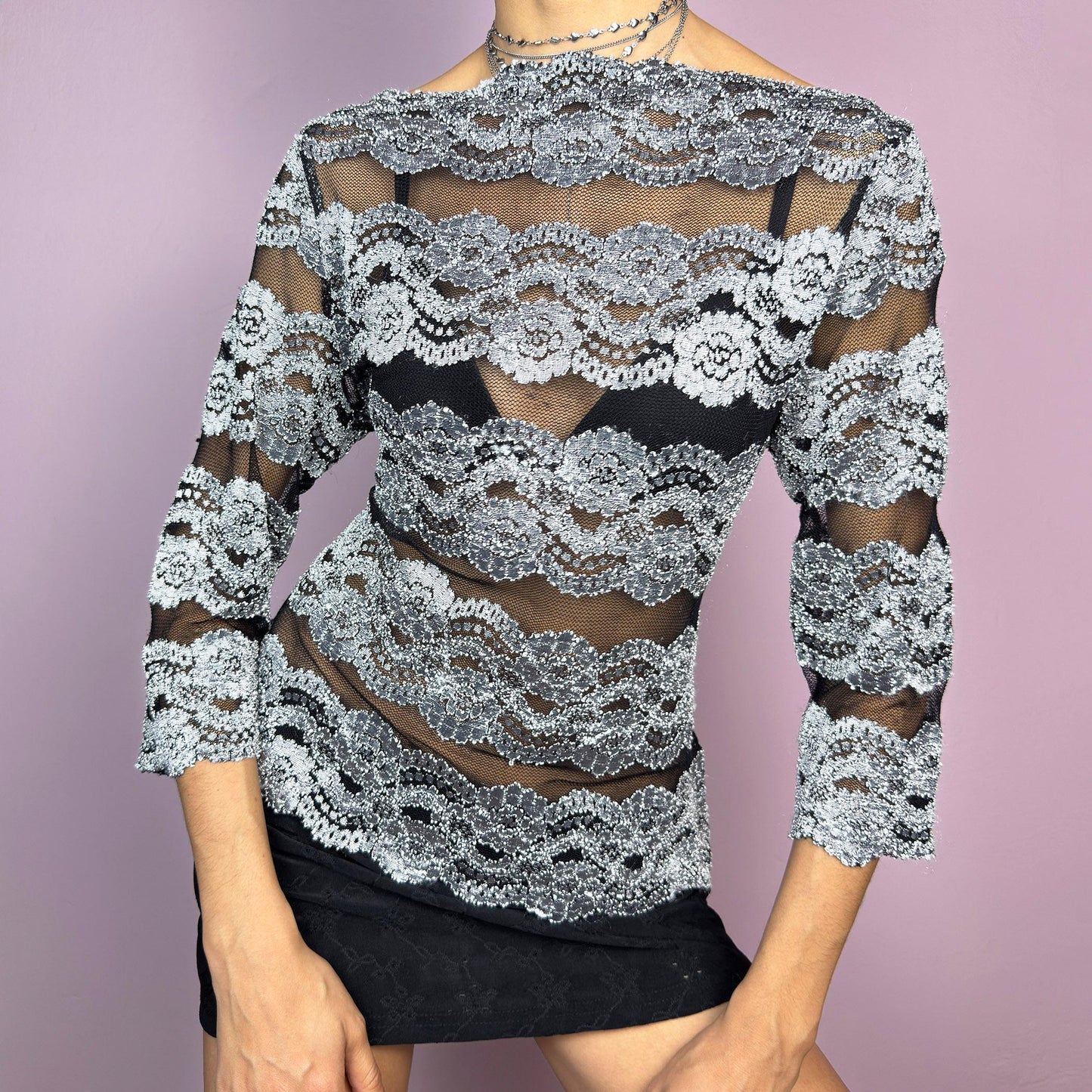 The Y2K Lace Mesh Black Top is a vintage 2000s statement sheer blouse featuring a delicate black mesh base with intricate silver lace embroidery in horizontal stripes. Designed with a fitted silhouette and three-quarter sleeves, this top is perfect for a romantic night or a bold evening outfit.