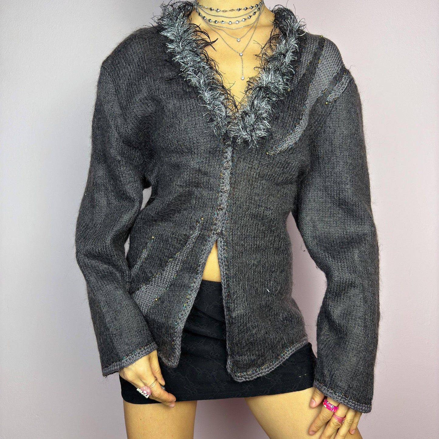 The Vintage 90s Gray Shaggy Trim Cardigan is a unique statement knitwear piece, featuring a soft knit fabric. Designed with a shaggy, hairy-textured trim along the V-neckline, subtle beaded embellishments, and button closure, this cardigan is perfect for cozy winter outfits. adult world shop