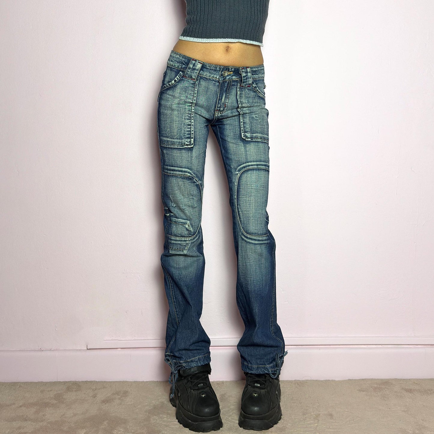 The Y2K Low-Rise Straight Jeans are a vintage 2000s piece featuring a rugged blue denim wash with contrast stitching and structured paneling. Designed with a flattering low-rise fit, straight-leg silhouette, knee patches, button and zipper closure, and adjustable drawstrings at the hems, these jeans offer a bold deconstructed utilitarian aesthetic. Perfect for edgy streetwear looks. adult world shop