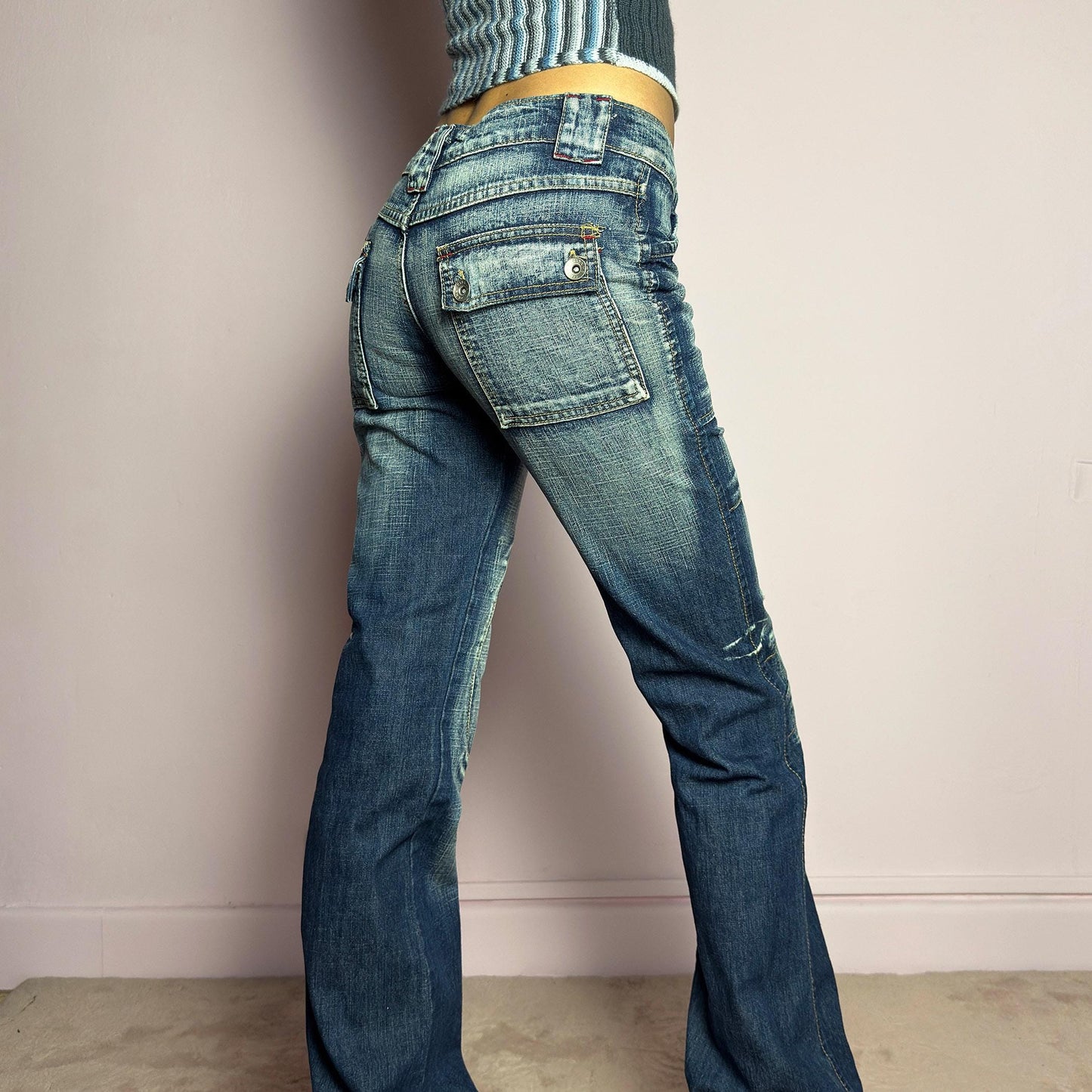 The Y2K Low-Rise Straight Jeans are a vintage 2000s piece featuring a rugged blue denim wash with contrast stitching and structured paneling. Designed with a flattering low-rise fit, straight-leg silhouette, knee patches, button and zipper closure, and adjustable drawstrings at the hems, these jeans offer a bold deconstructed utilitarian aesthetic. Perfect for edgy streetwear looks. adult world shop